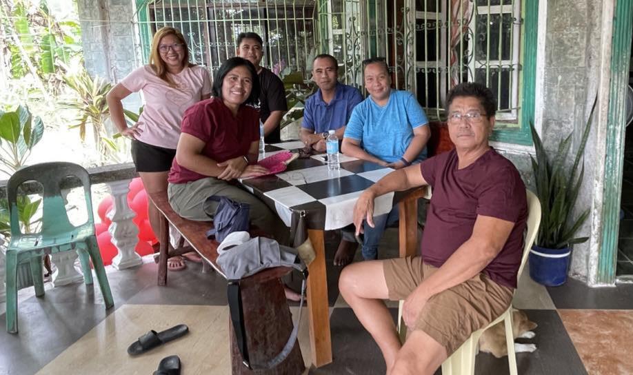 Six people enjoy a relaxed time together at a house surrounded by greenery.