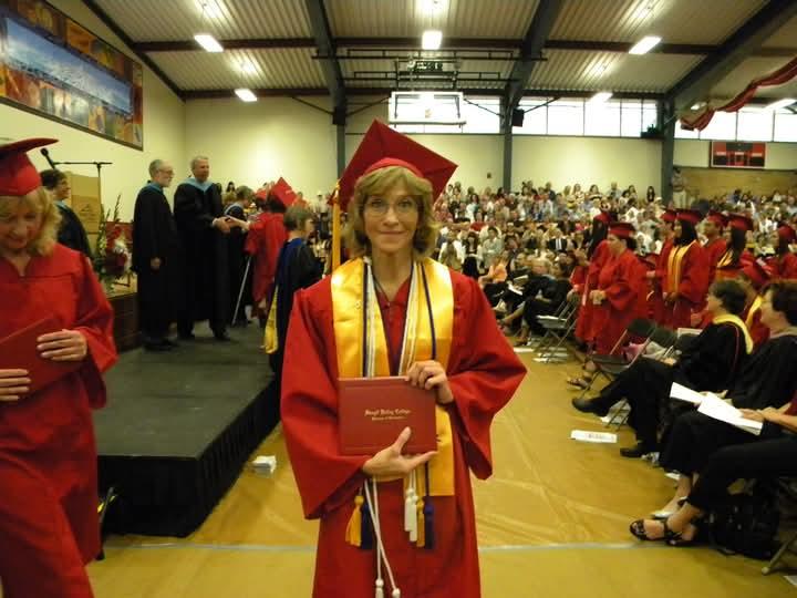 Graduates in red gowns celebrate receiving diplomas while an audience cheers in a large venue.