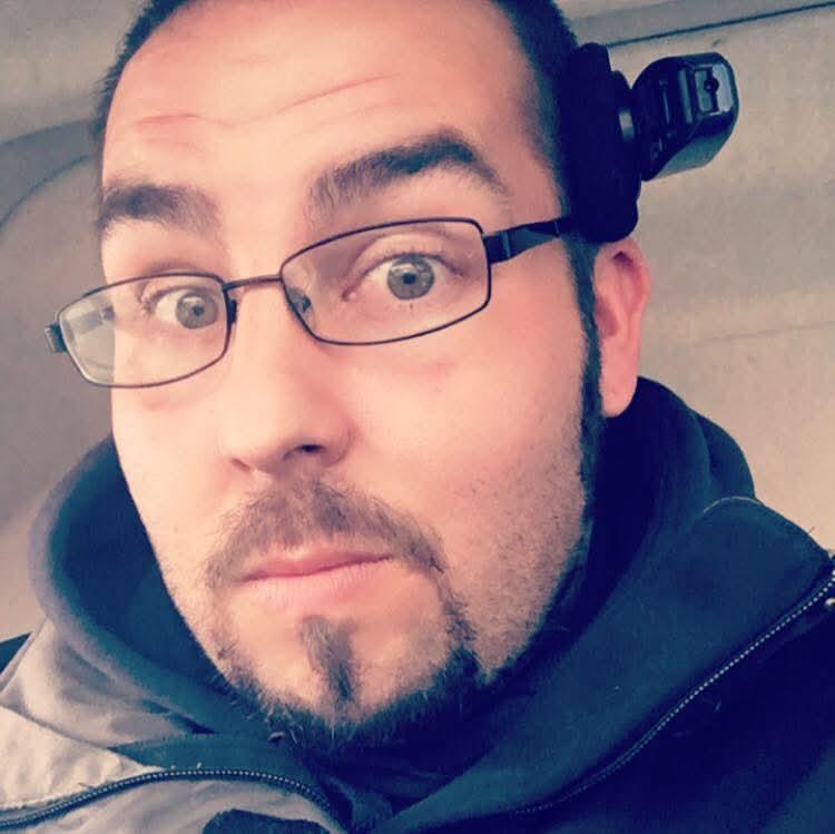 A man with glasses shows a surprised expression while inside a car.