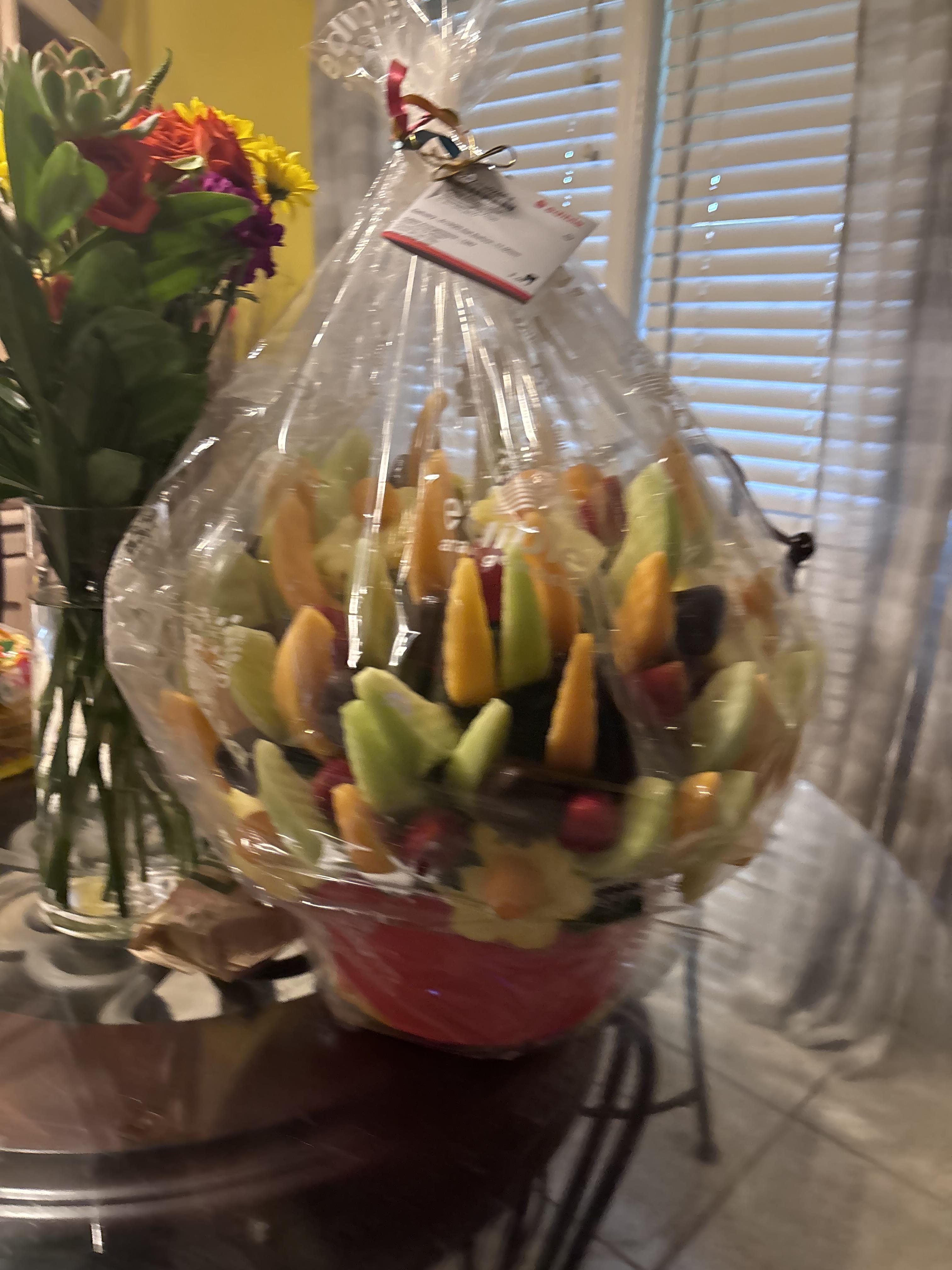 An elegant fruit bouquet is showcased on a table, surrounded by vibrant floral arrangements.