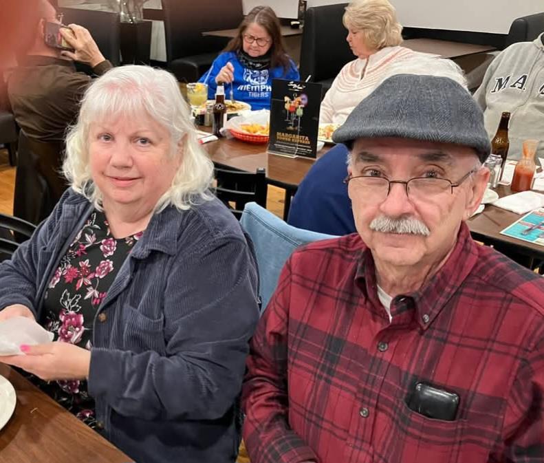An elderly couple sits at a restaurant table, enjoying their time with friends during dinner.