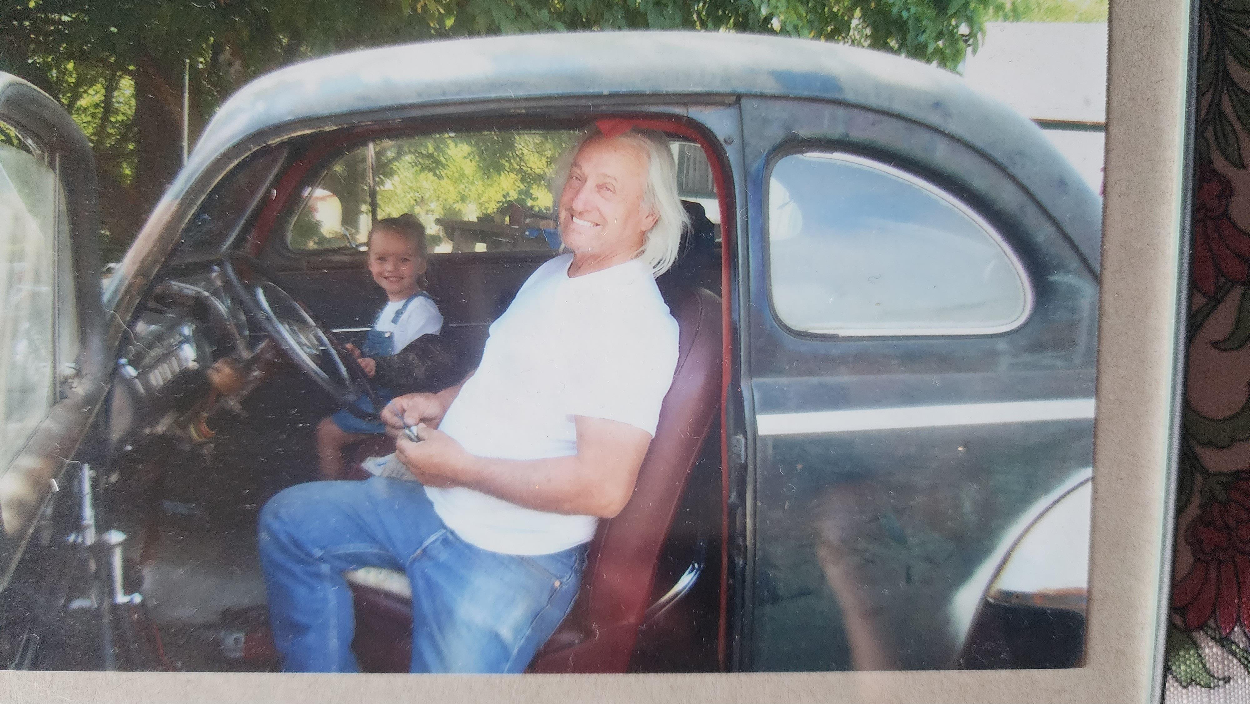 A joyful man sits in a classic car while a child smiles beside him, creating a warm moment.