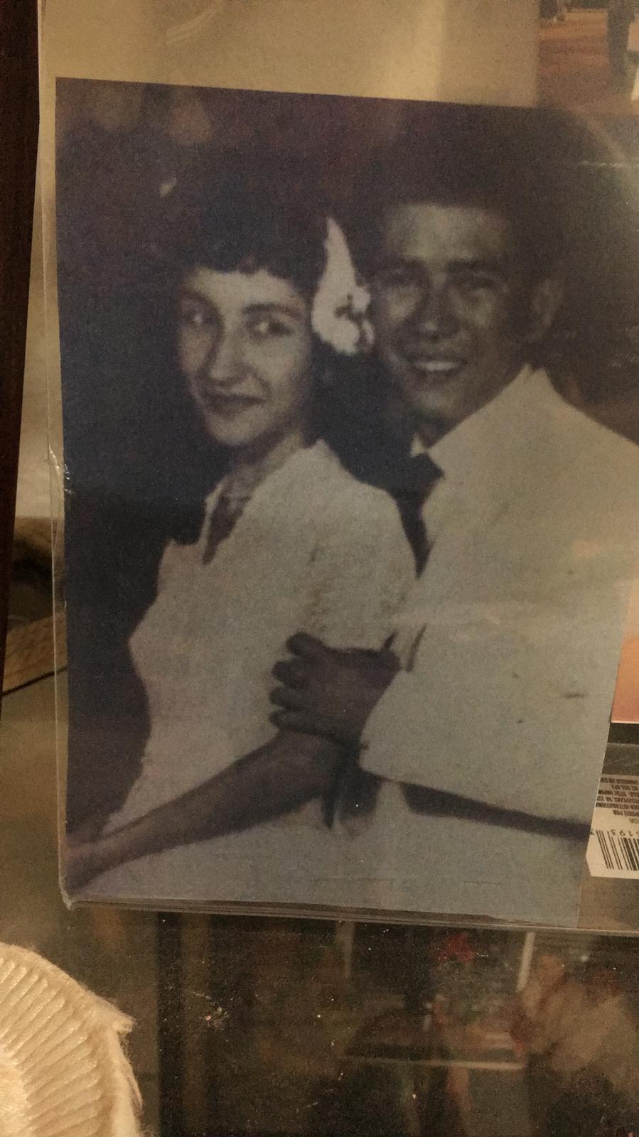 A young couple poses closely together at a formal gathering in the past, smiling warmly.