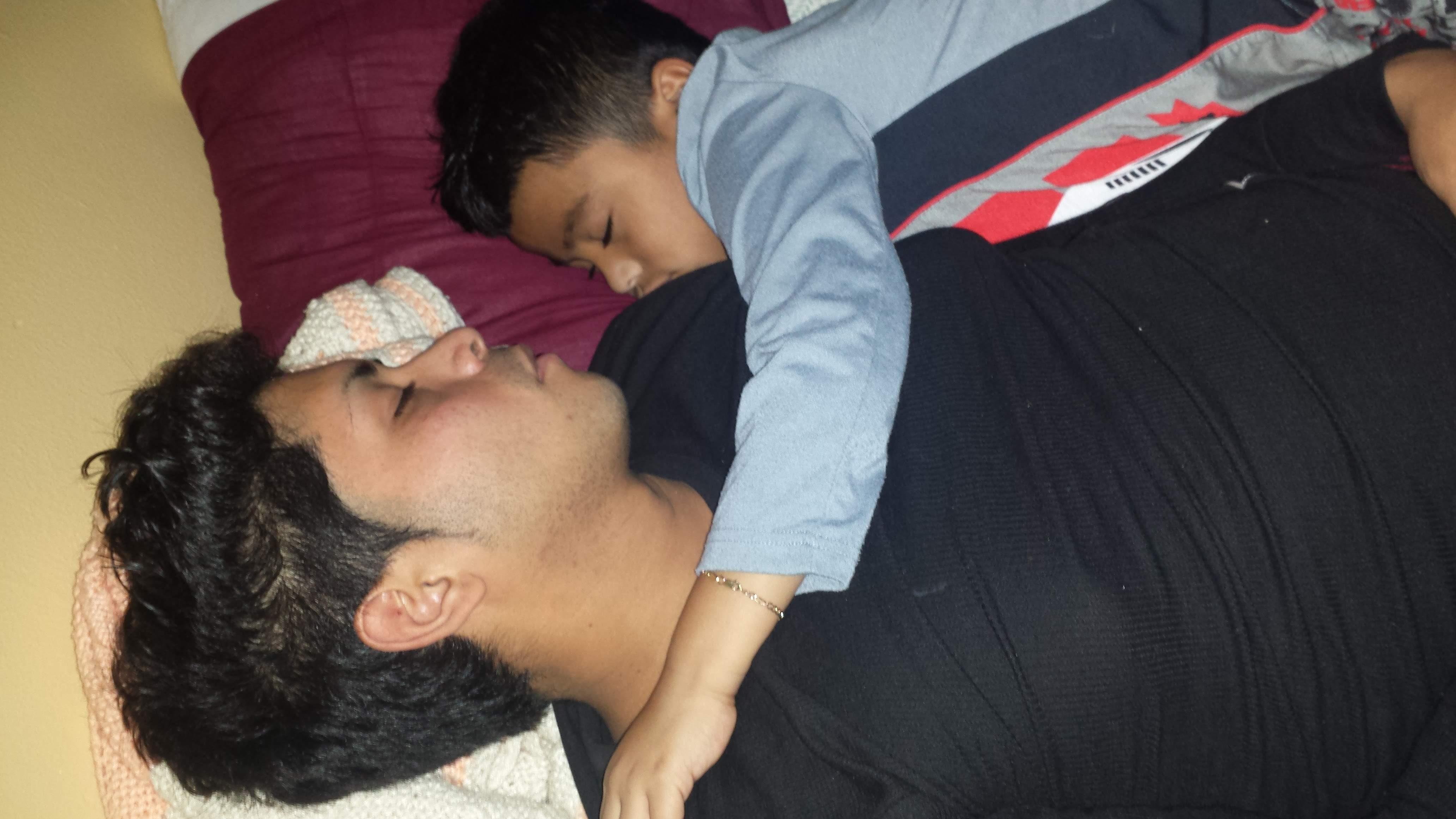 A father cuddles with his young son, sharing a peaceful moment as they sleep.