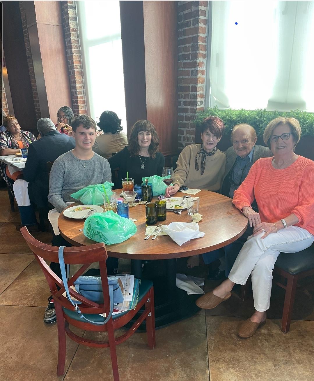 Five friends gather around a table, sharing a meal and enjoying each other's company at lunch time.