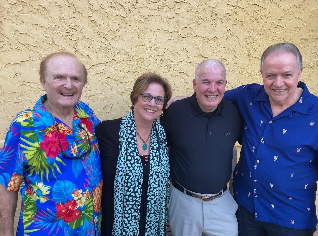 Four friends gather outdoors against a bright yellow wall, sharing smiles and warmth on a sunny day.