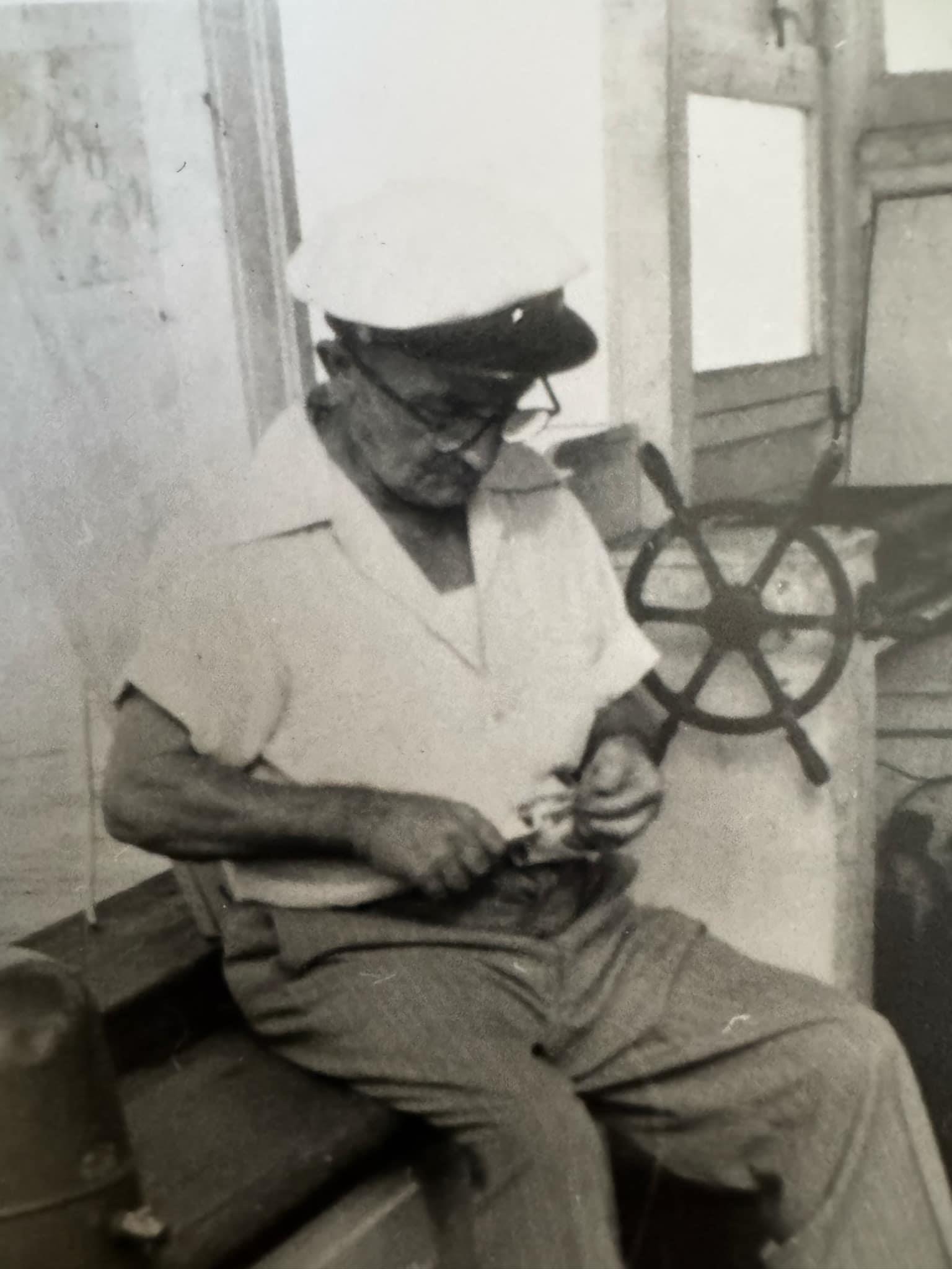 An elderly man is working on a small wooden item, surrounded by nautical elements inside a boat.