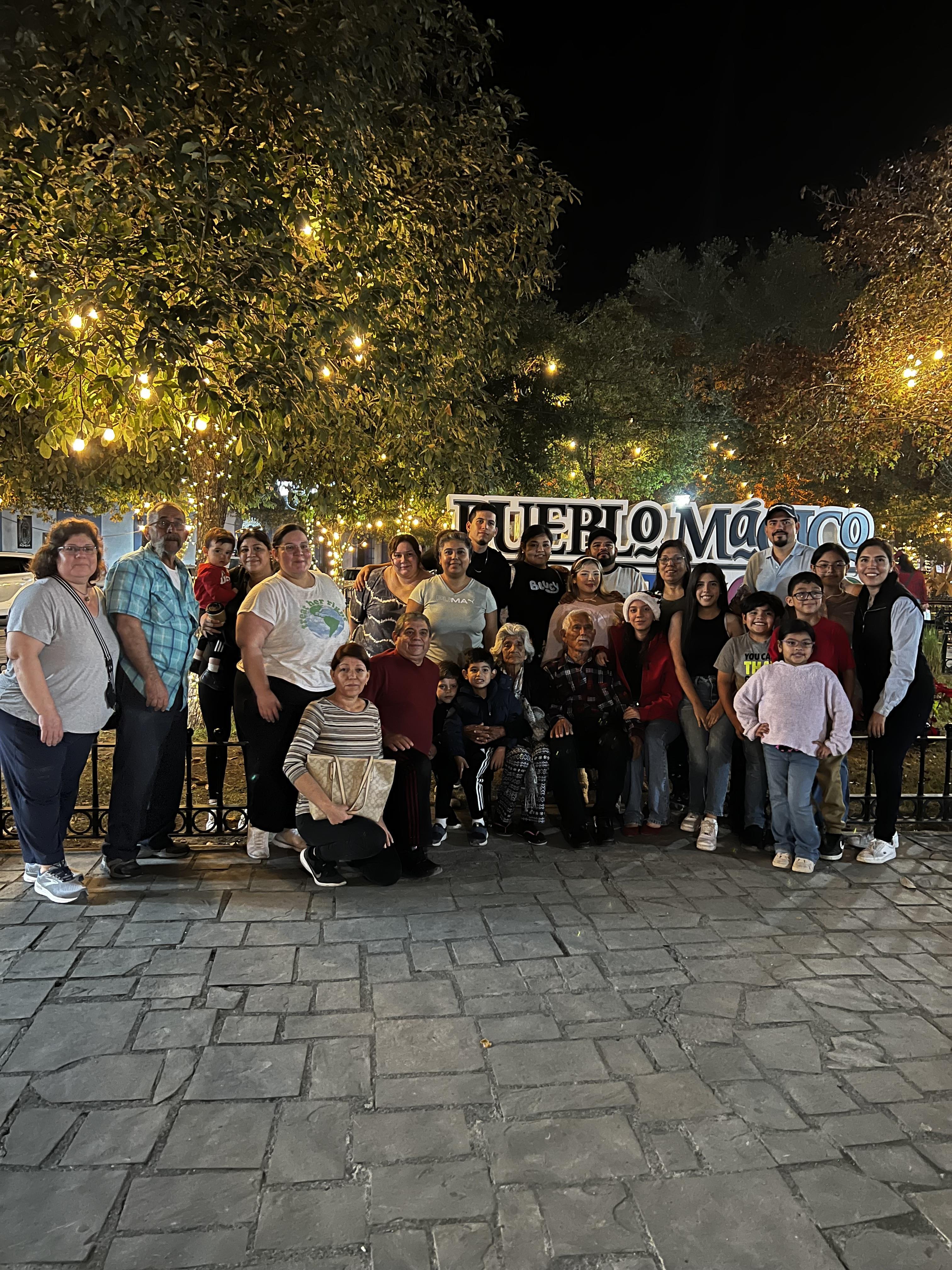 A large family enjoys a night gathering in Pueblo Magico, surrounded by vibrant lights.