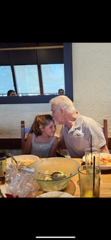 Grandfather playfully interacts with his granddaughter while enjoying a meal together at a table.