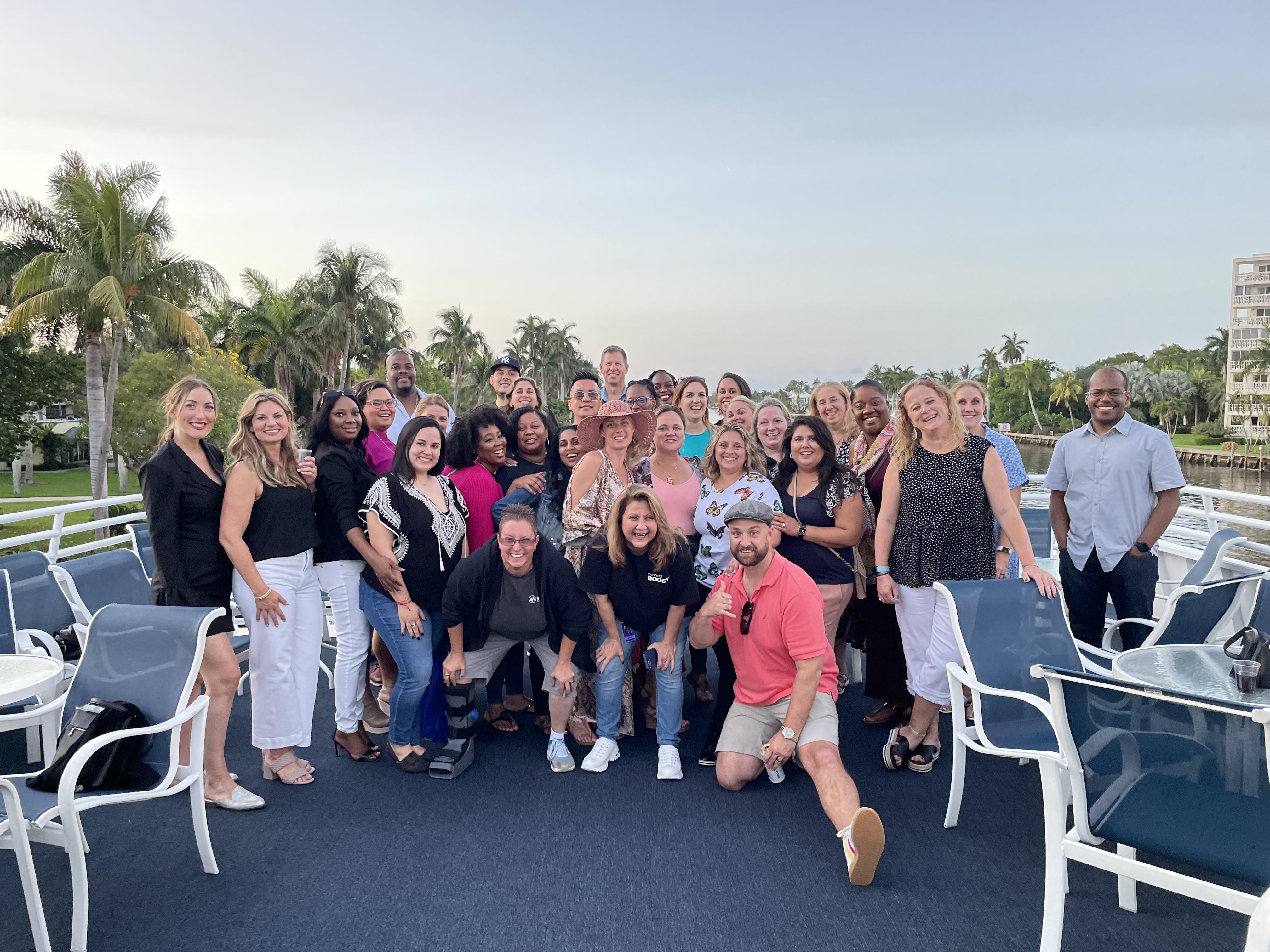 A large group of people celebrates together on a boat at sunset, enjoying each other's company.