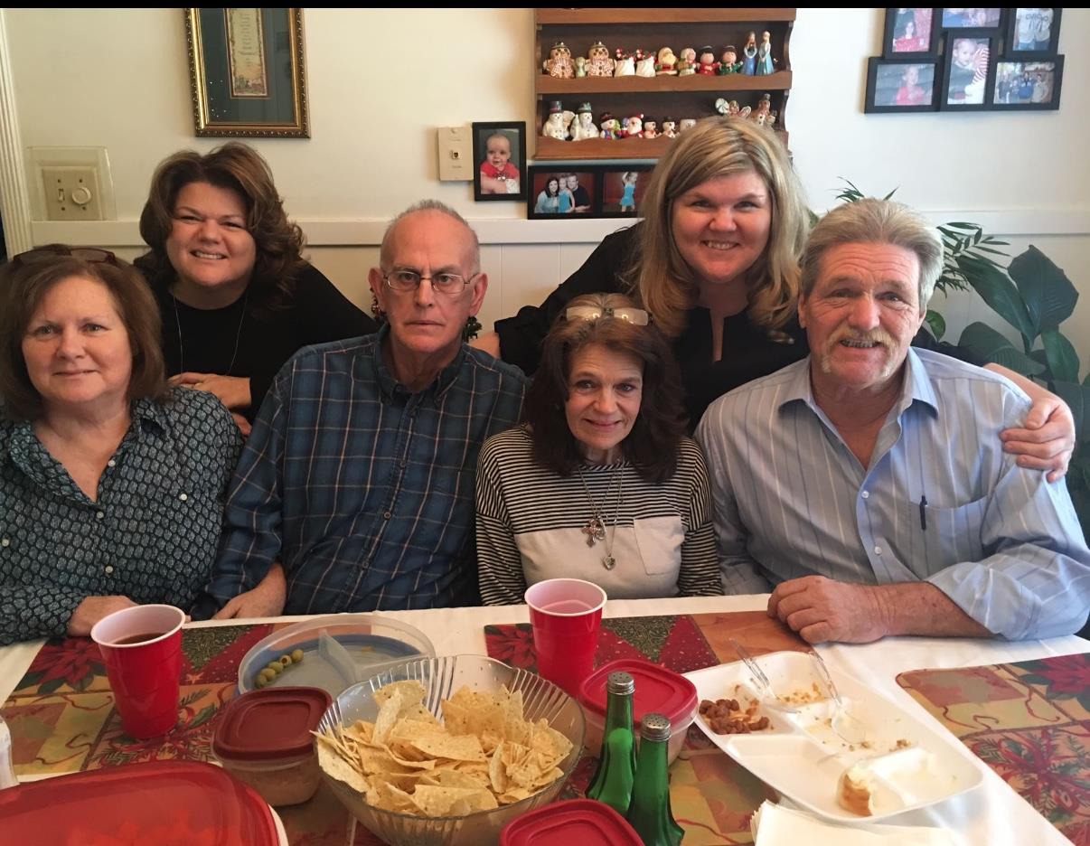 Family members smile together around a table filled with snacks in a warm and inviting home.