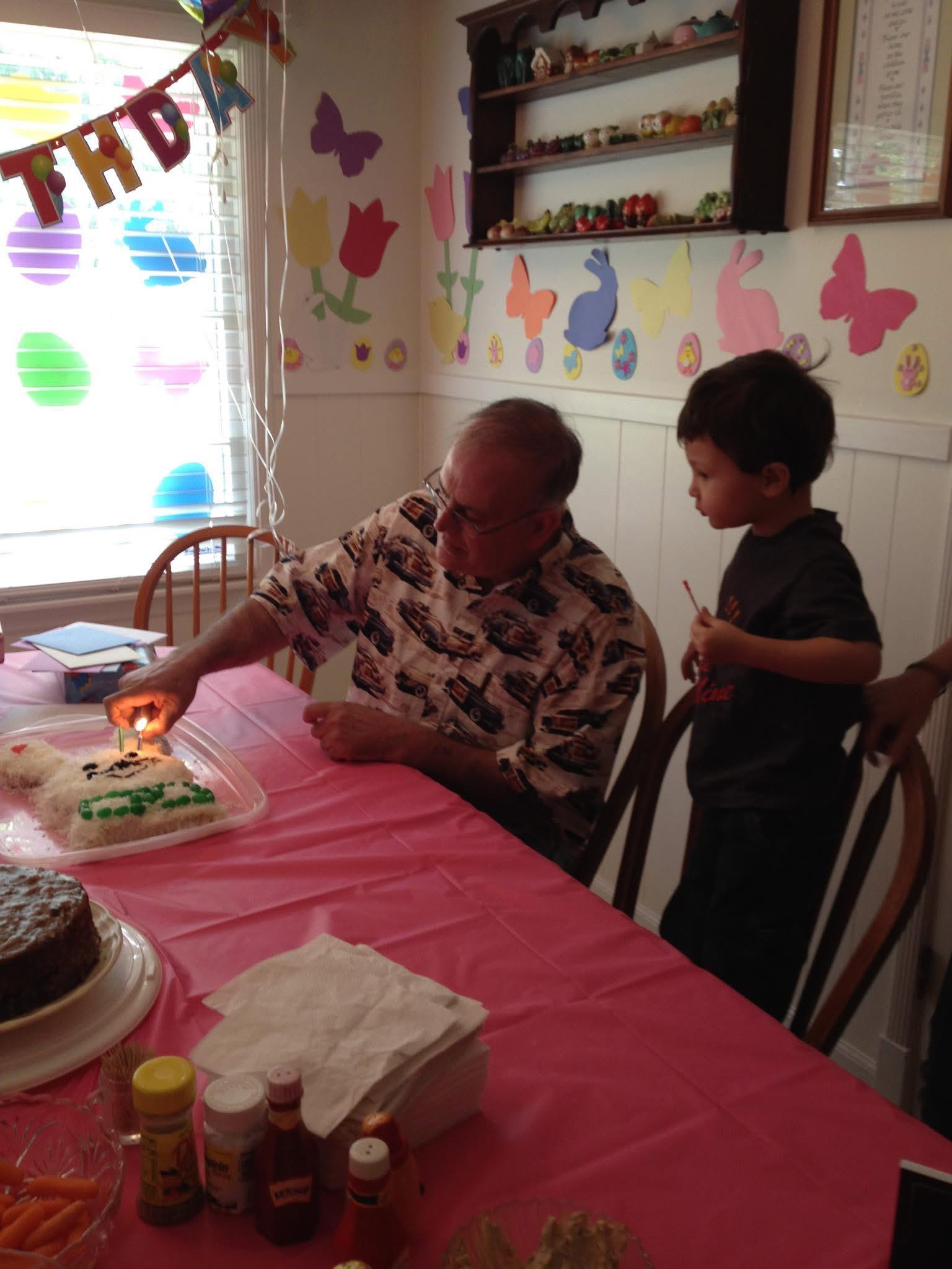 A boy stands beside his grandfather as they prepare to light a birthday candle on a cake.