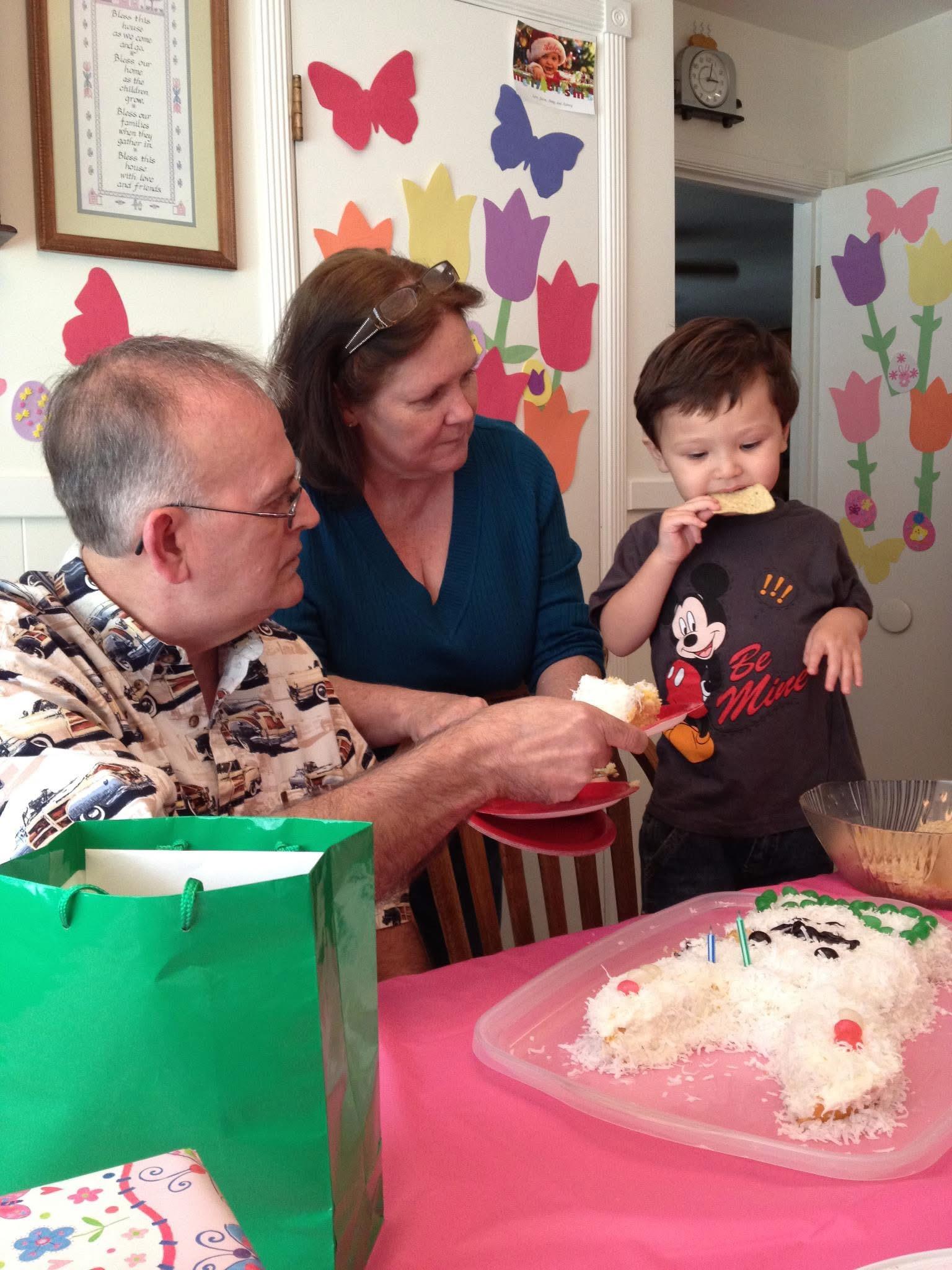 A young boy celebrates his birthday with cake, family, decorations, and gifts.