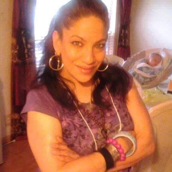 A confident woman is smiling while posing in her living room with a baby in a crib.