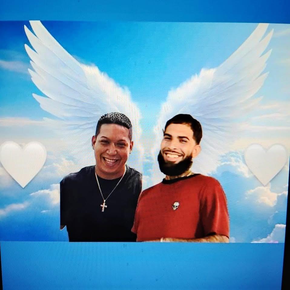 Two men stand together, smiling joyfully, with a serene sky and angel wings behind them.