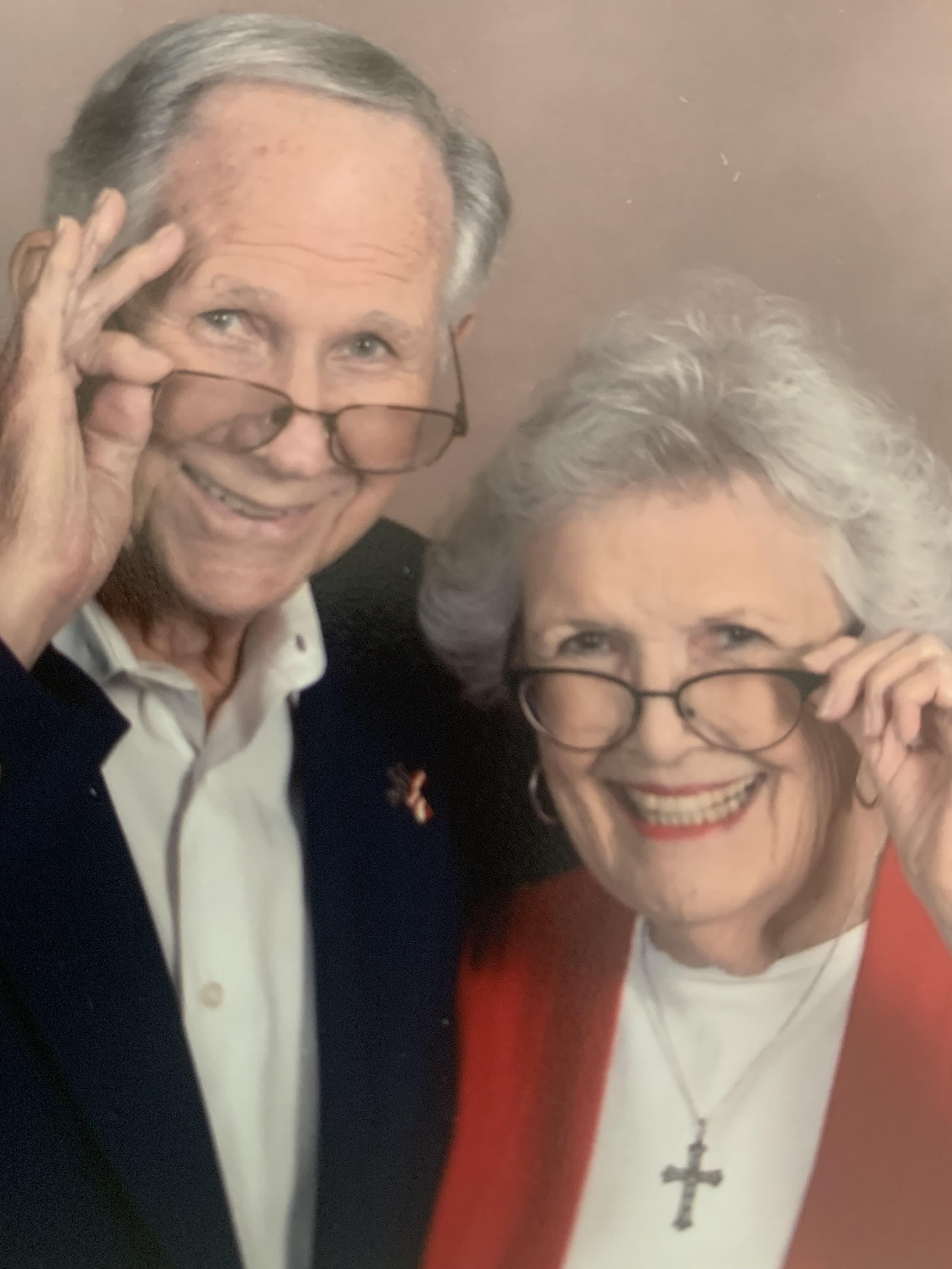 Joyful elderly couple shows affection while playfully adjusting their glasses, smiling brightly.