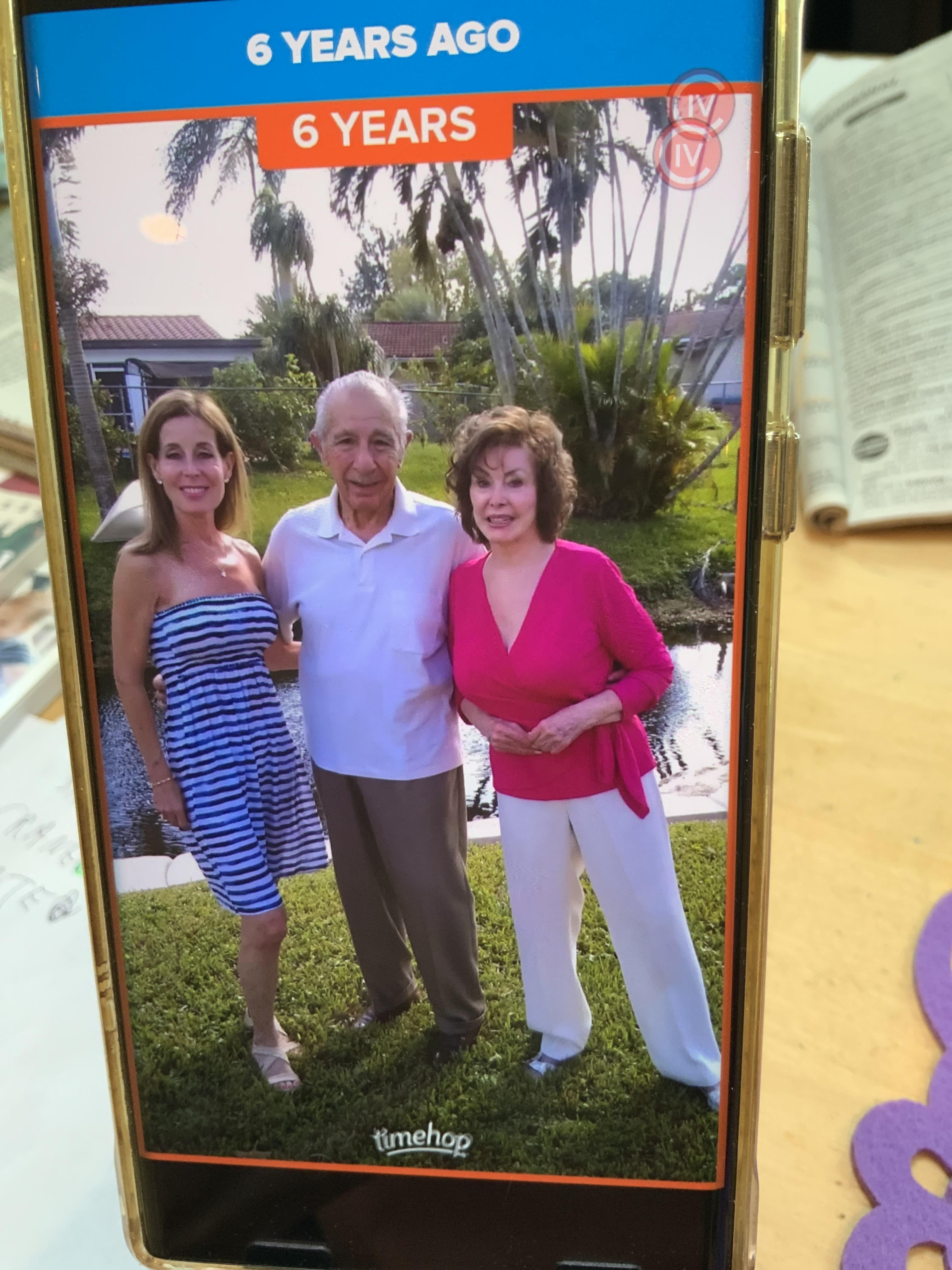 Three people pose together with smiles near a picturesque waterway surrounded by greenery.