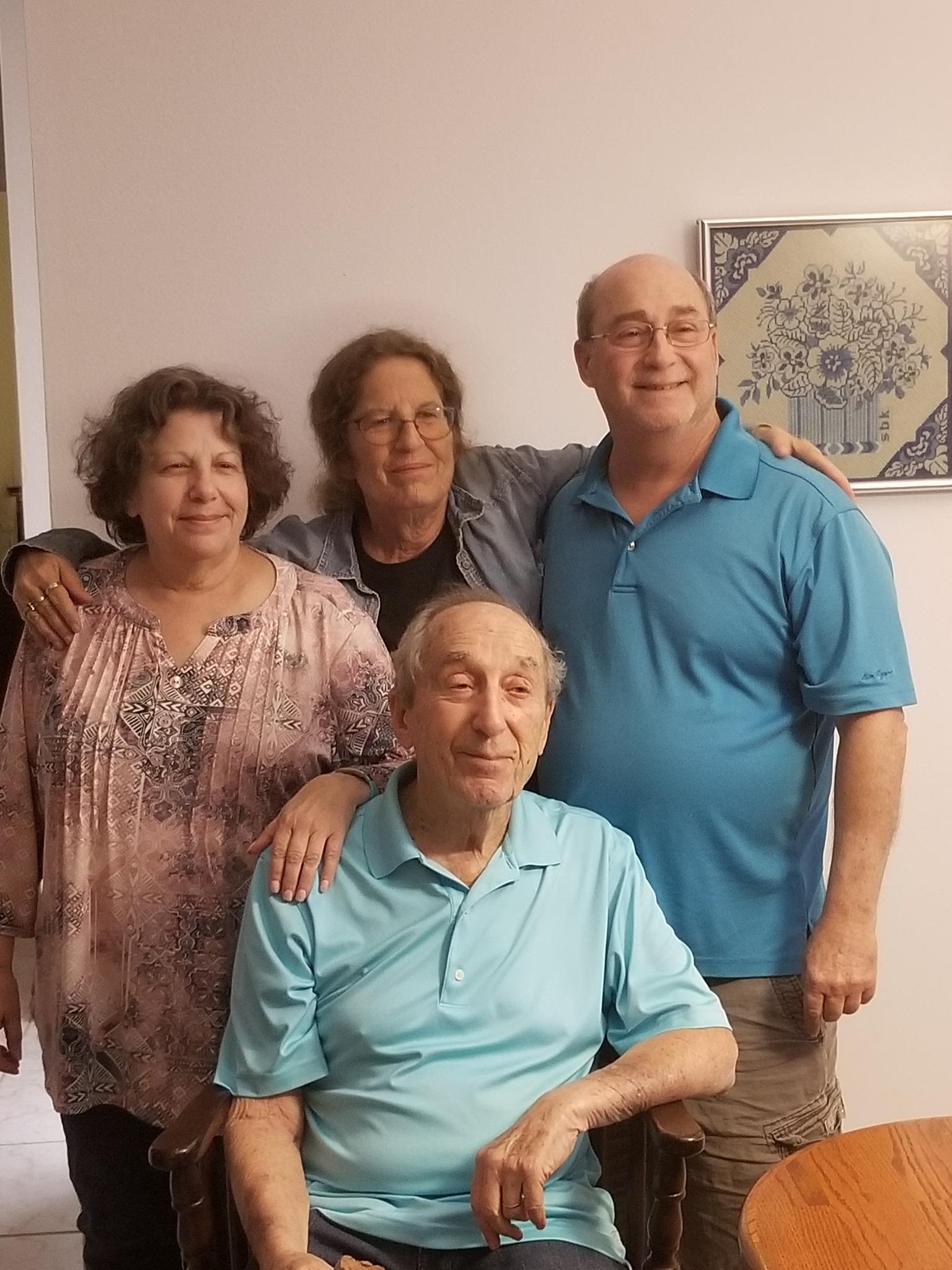 Two women and two men stand together, smiling warmly in a comfortable interior setting.