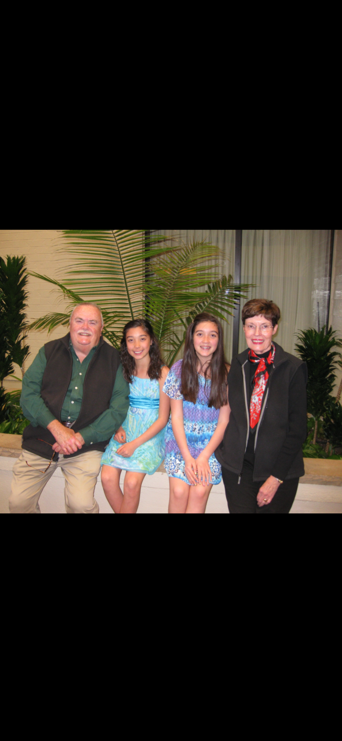 Two girls with long hair pose in bright dresses alongside two adults in a cozy indoor space.