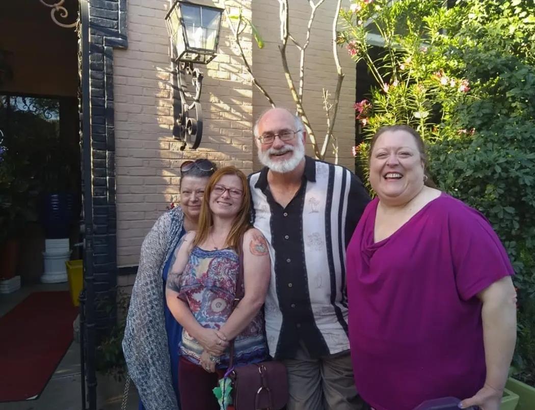 Four friends smile together in front of a charming house on a sunny day.