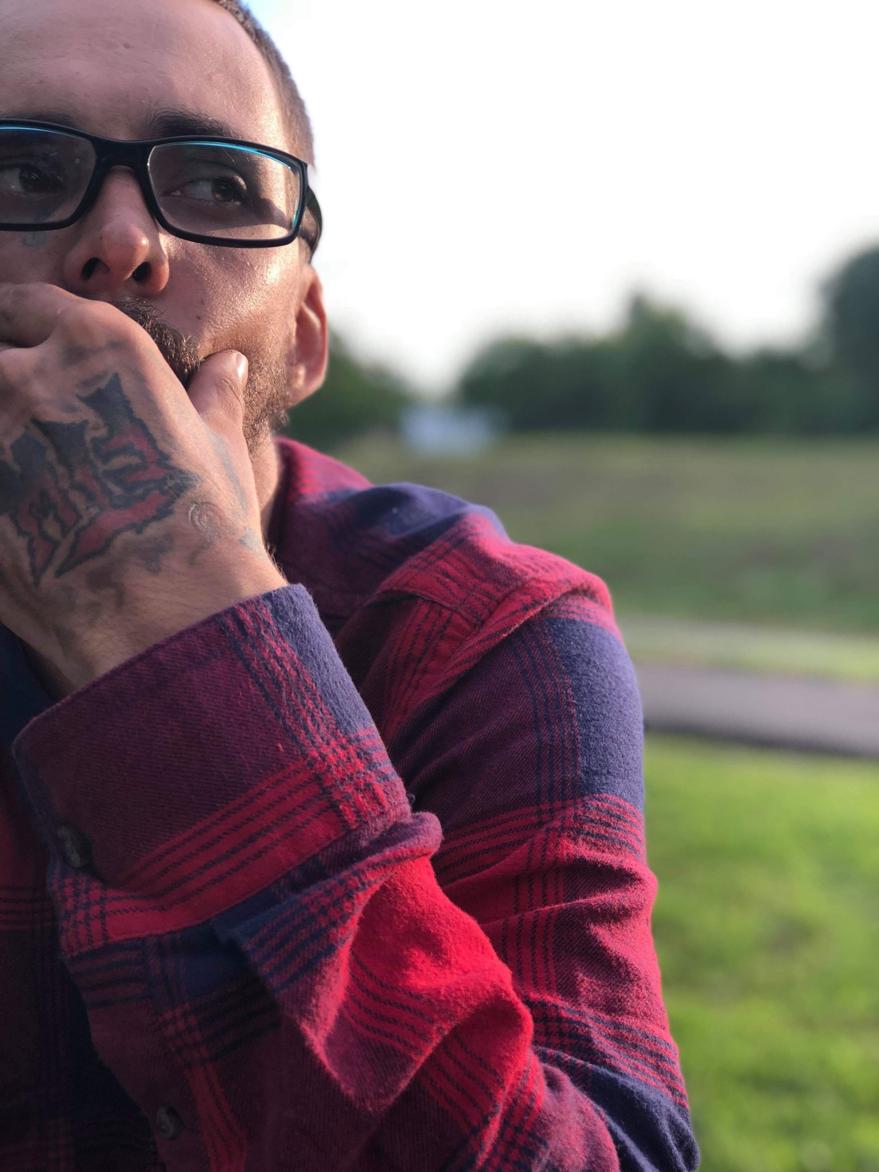 Man looks contemplative while sitting in a grassy area, surrounded by nature at dusk.