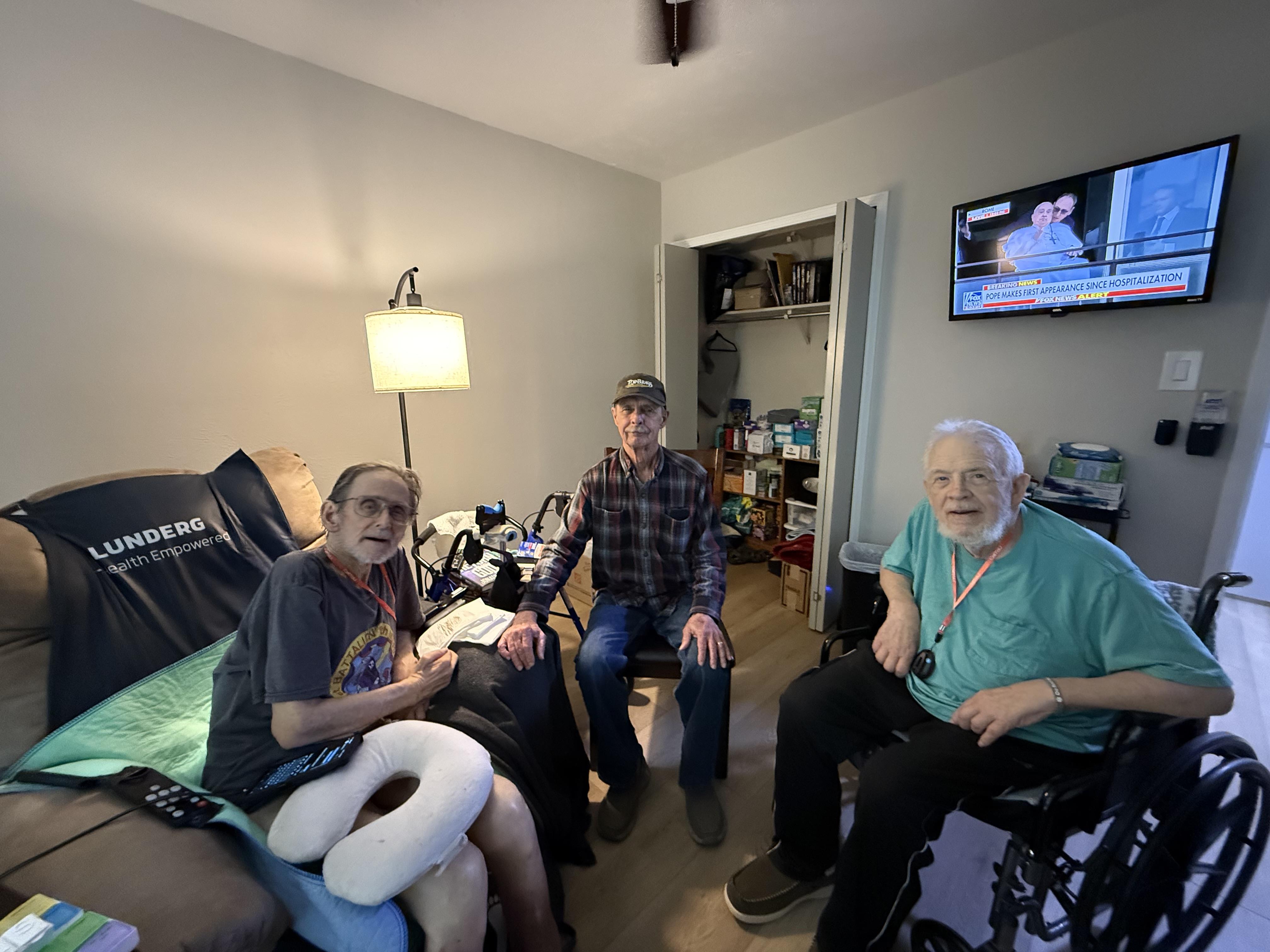 Three senior men sit together in a comfortable living space, sharing stories and laughter.