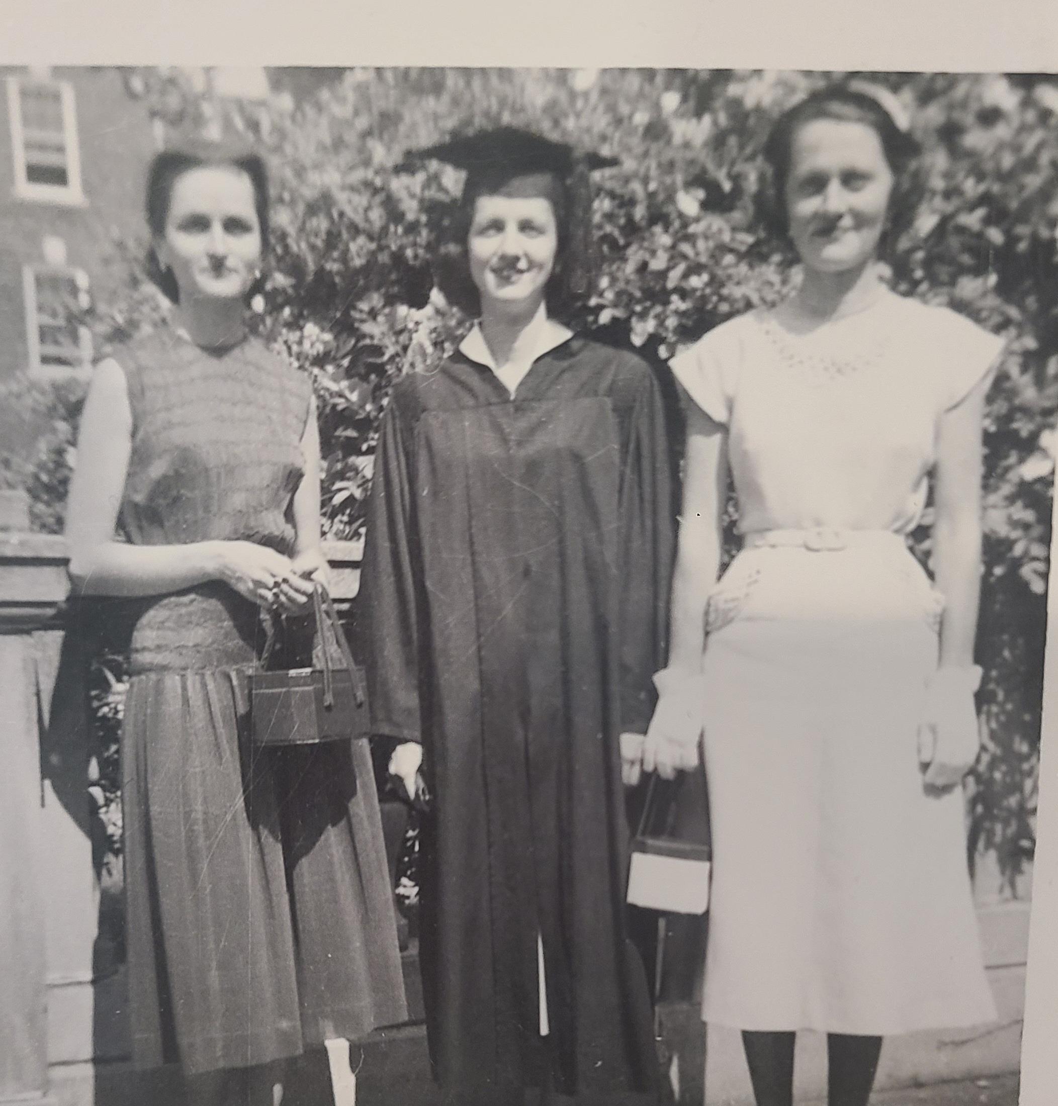 Three women gather to celebrate graduation outdoors, showcasing vintage fashion and accessories.