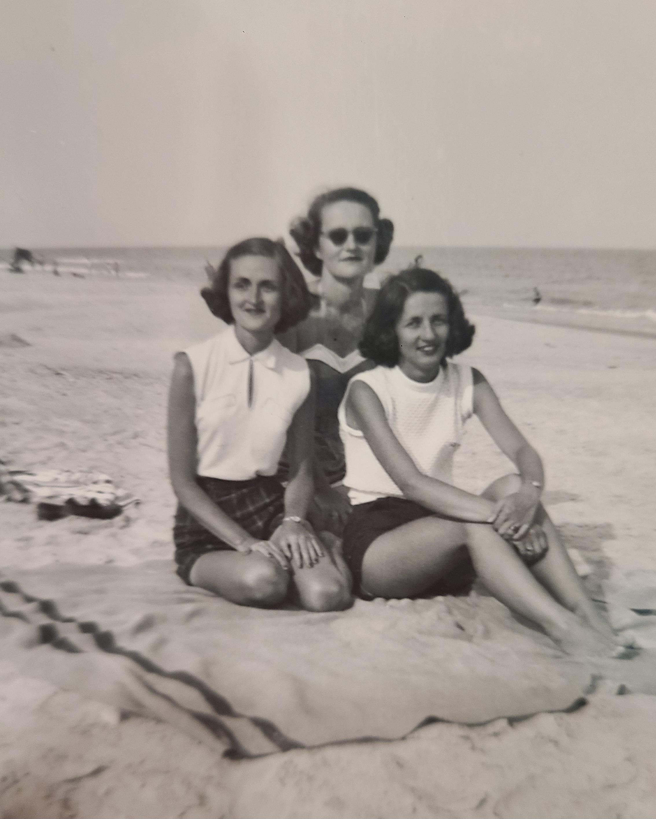 Three friends in 1940s beachwear relax on a blanket at the beach.