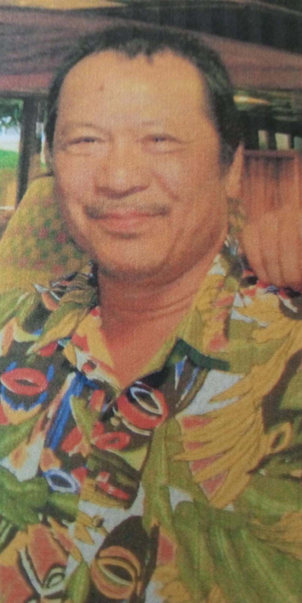 A man with a friendly smile poses wearing a vibrant shirt surrounded by tropical scenery.