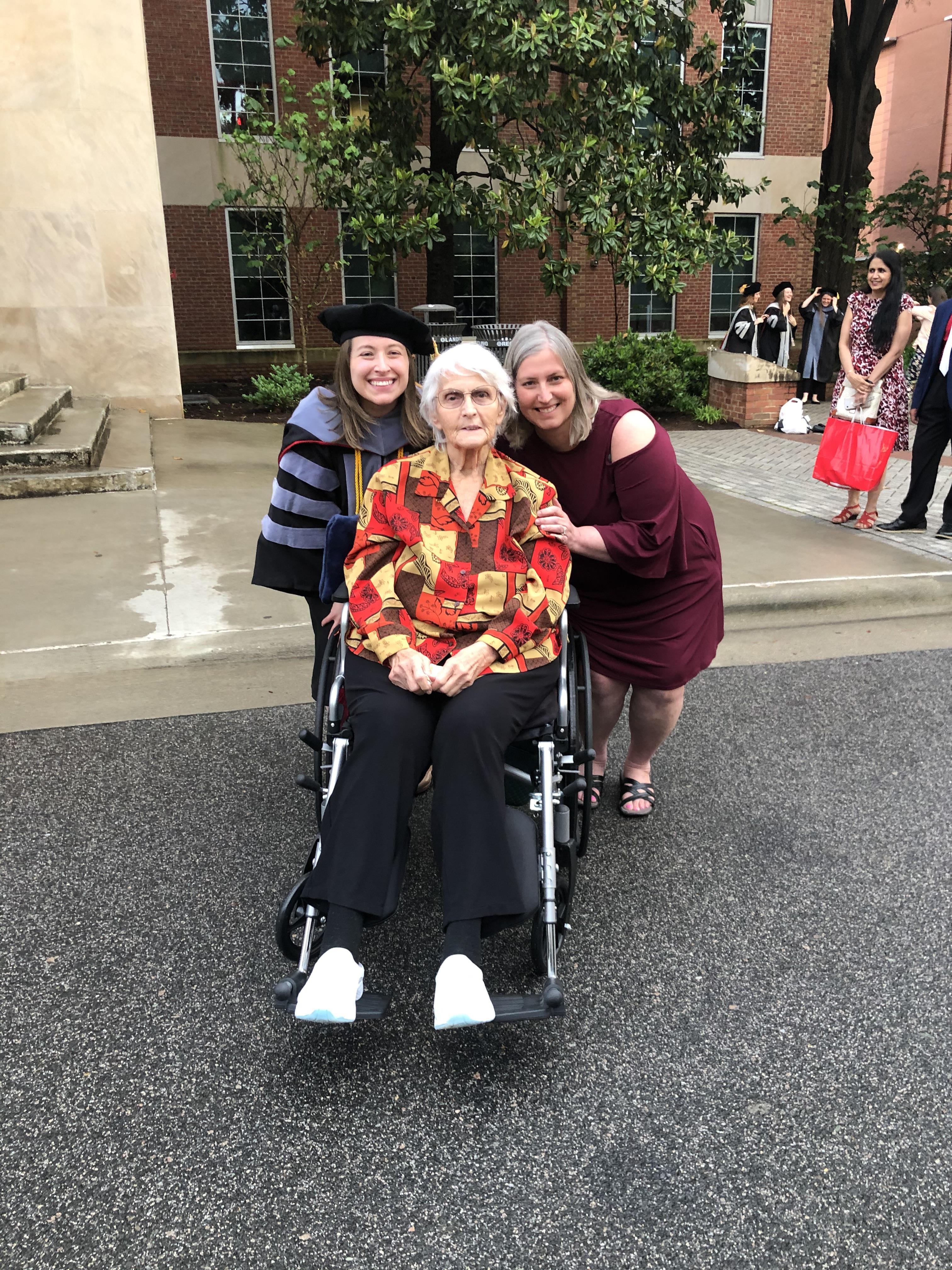 Graduates pose with their grandmother in a wheelchair during a university celebration.