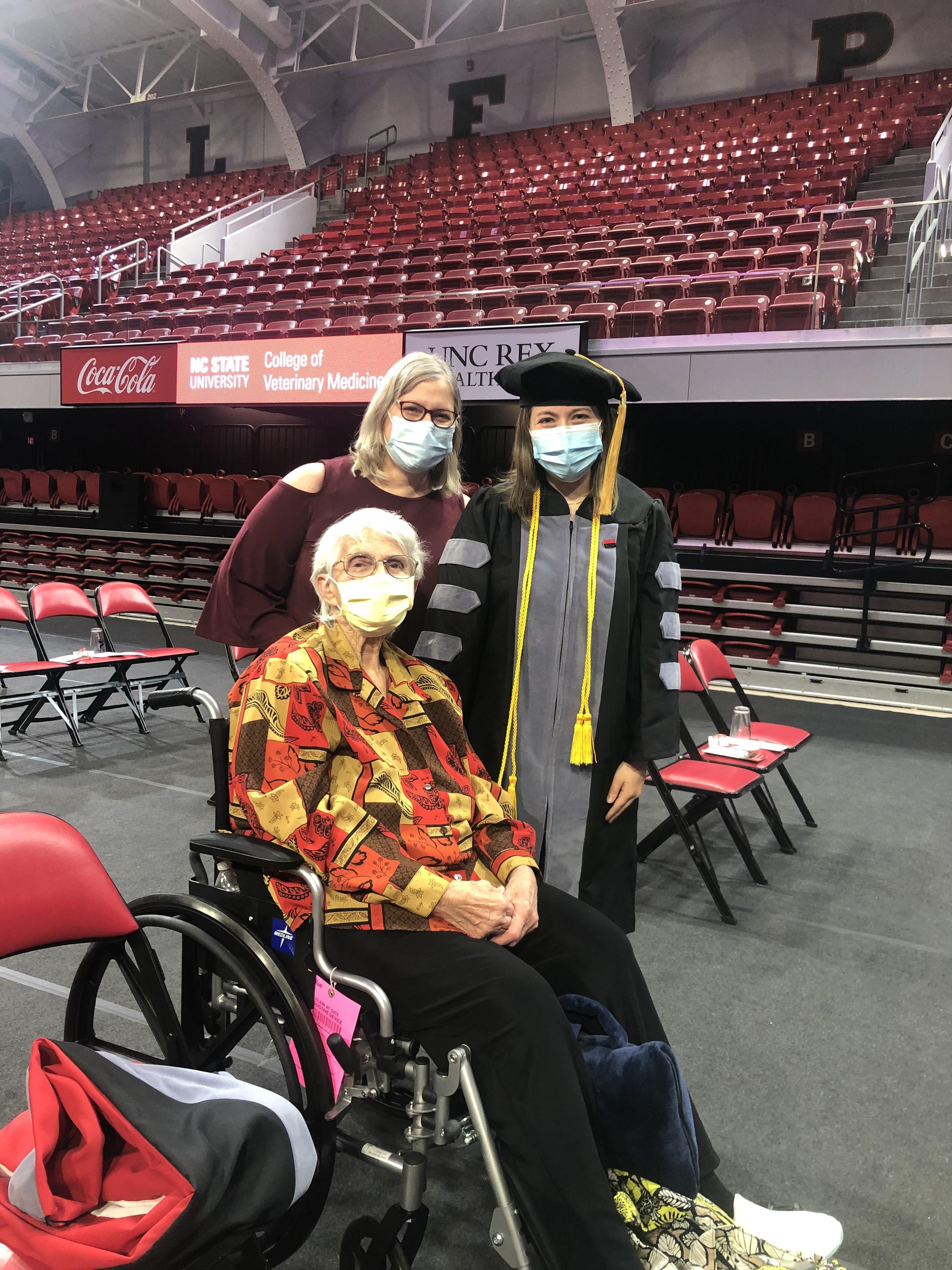 A smiling graduate poses proudly with two family members during a university commencement ceremony.