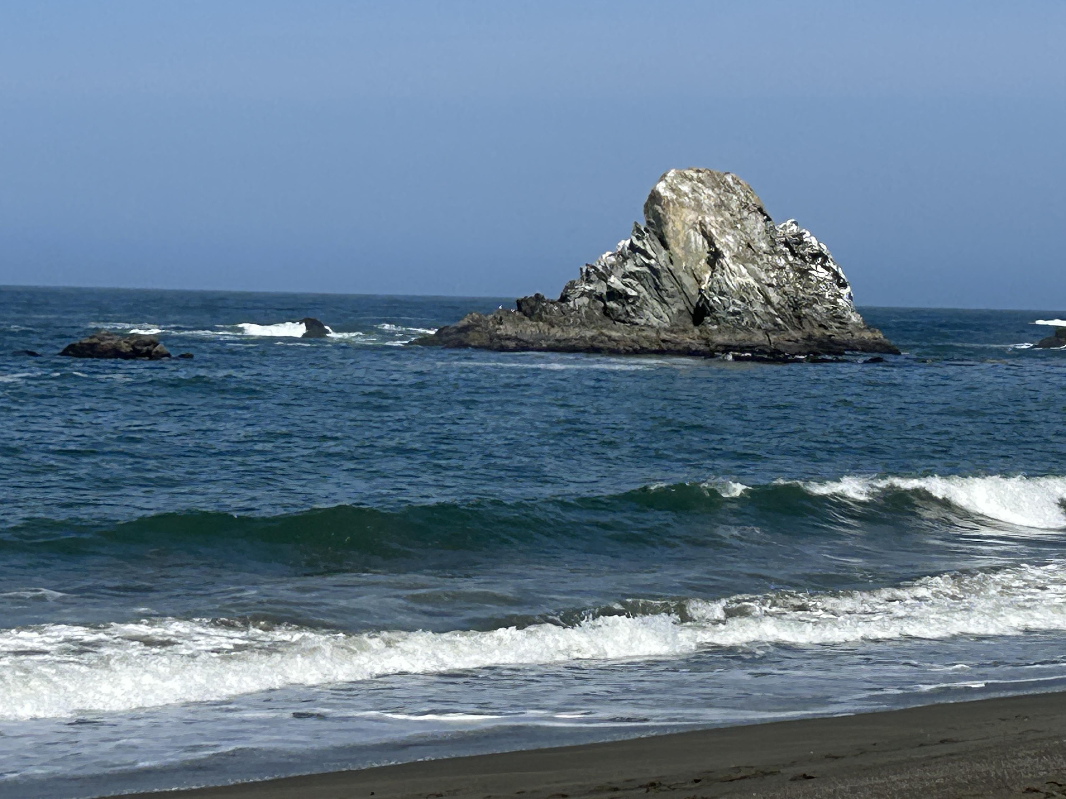 A rocky formation rises from the ocean, while soft waves lap against the sandy shore.