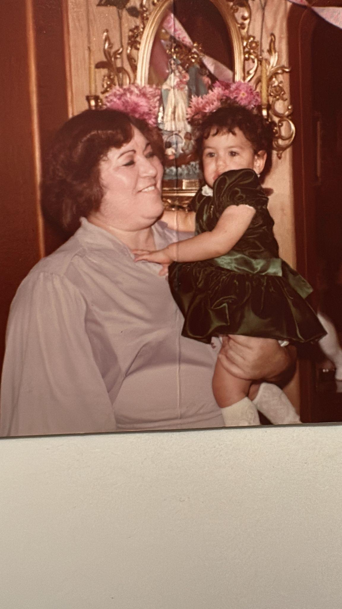 Grandmother holds her granddaughter in a cozy setting, both smiling amidst a festive atmosphere.