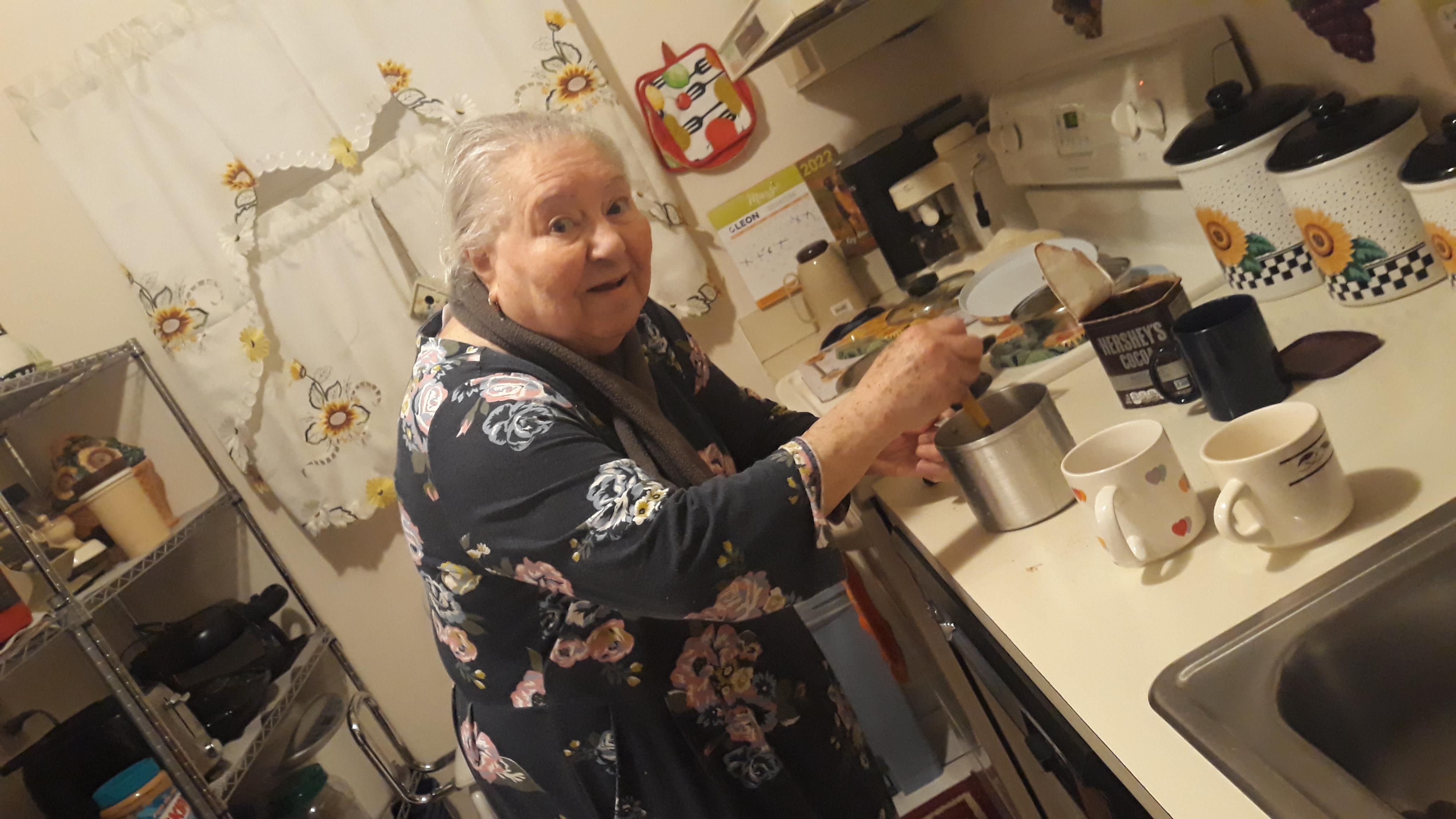 An elderly woman joyfully prepares a meal in her inviting kitchen filled with personal touches.
