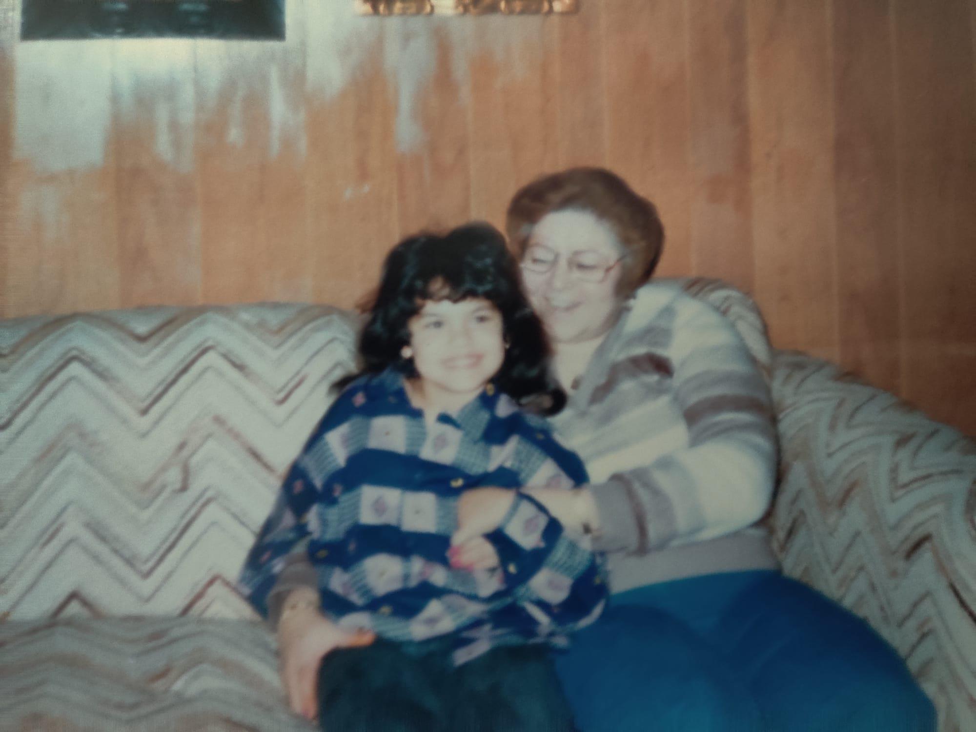 A child smiles on a vintage couch with a grandmother in a cozy living room.