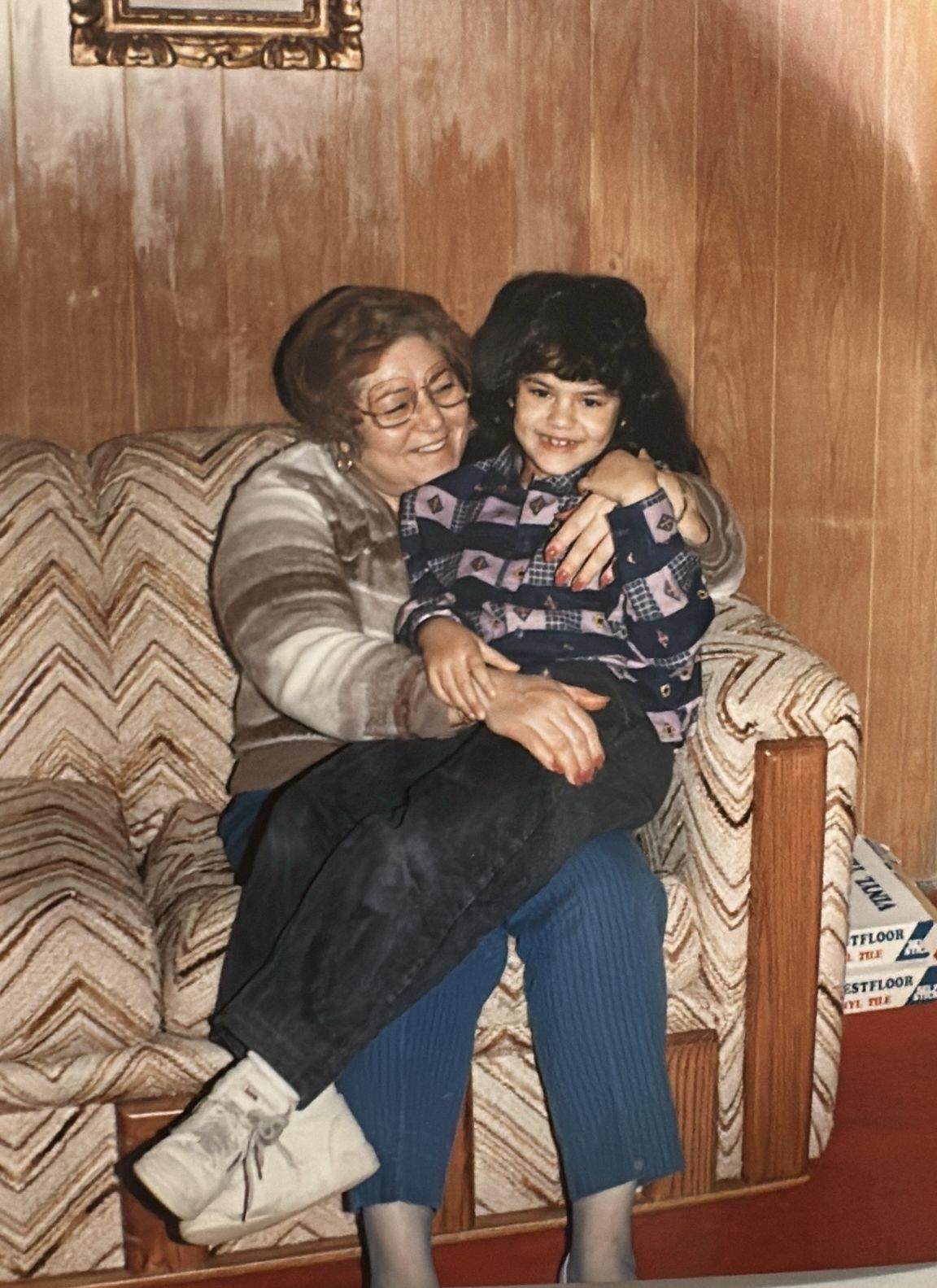 A loving grandmother embraces her granddaughter with joy while seated on a couch.