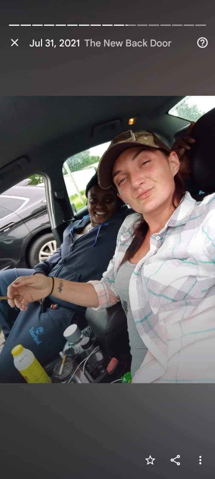 Two friends are seated inside a car, sharing a light moment together in warm weather.