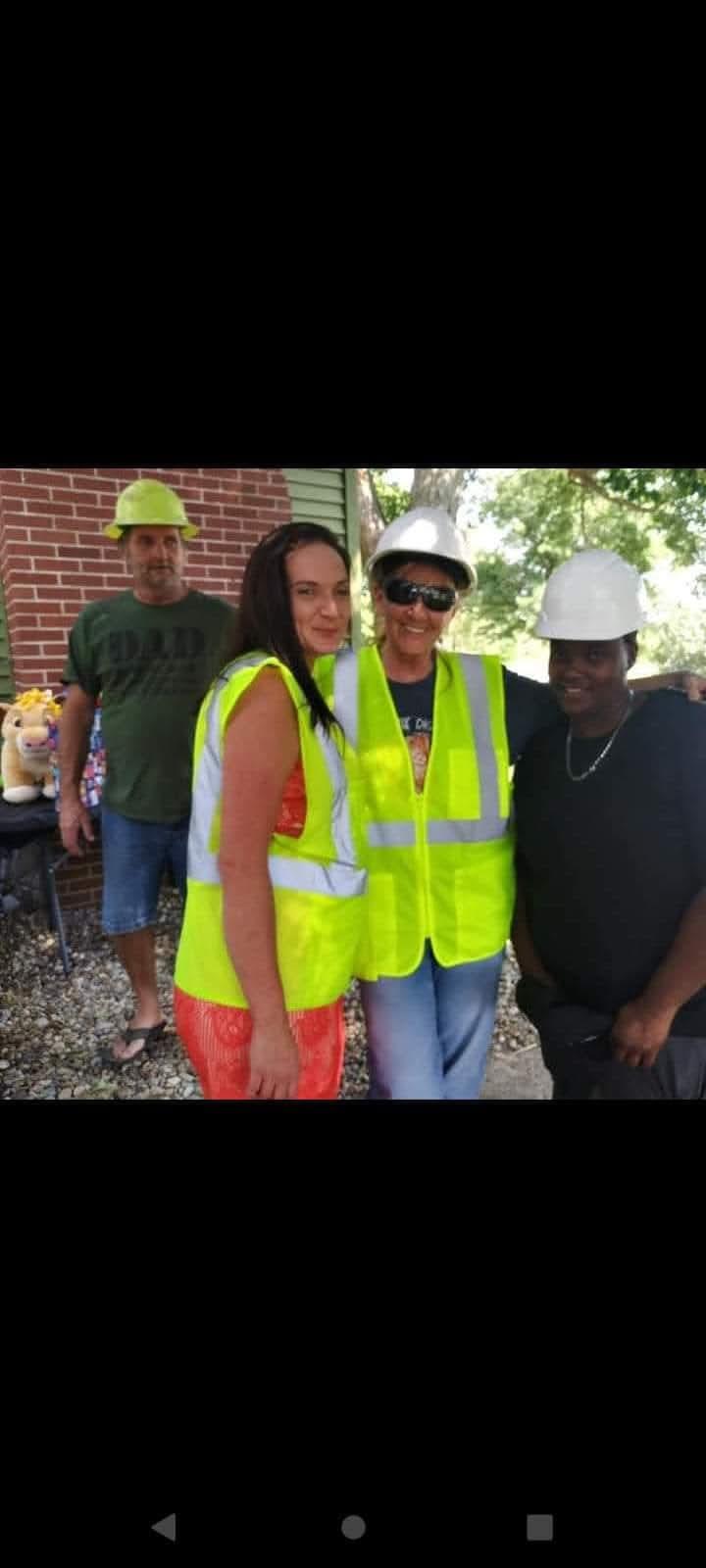 Friends enjoy a cheerful moment together at an outdoor gathering wearing safety vests and helmets.