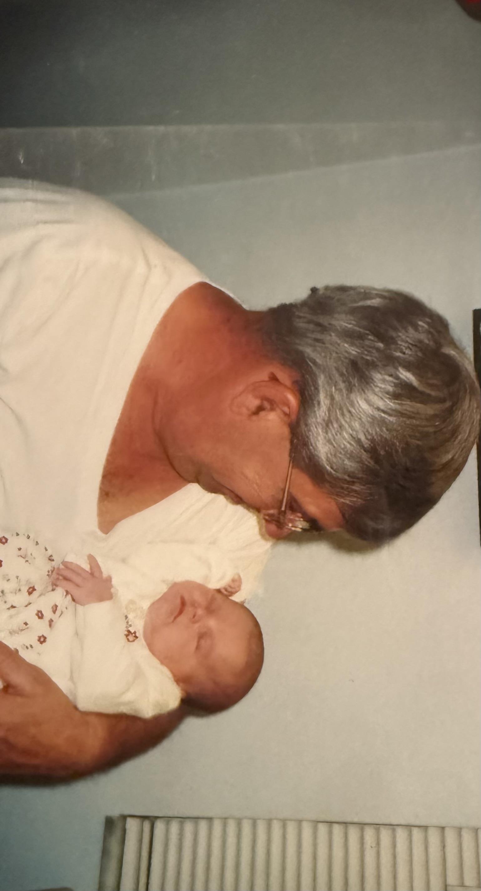 A grandfather cradles his peaceful newborn grandchild, sharing a loving moment.