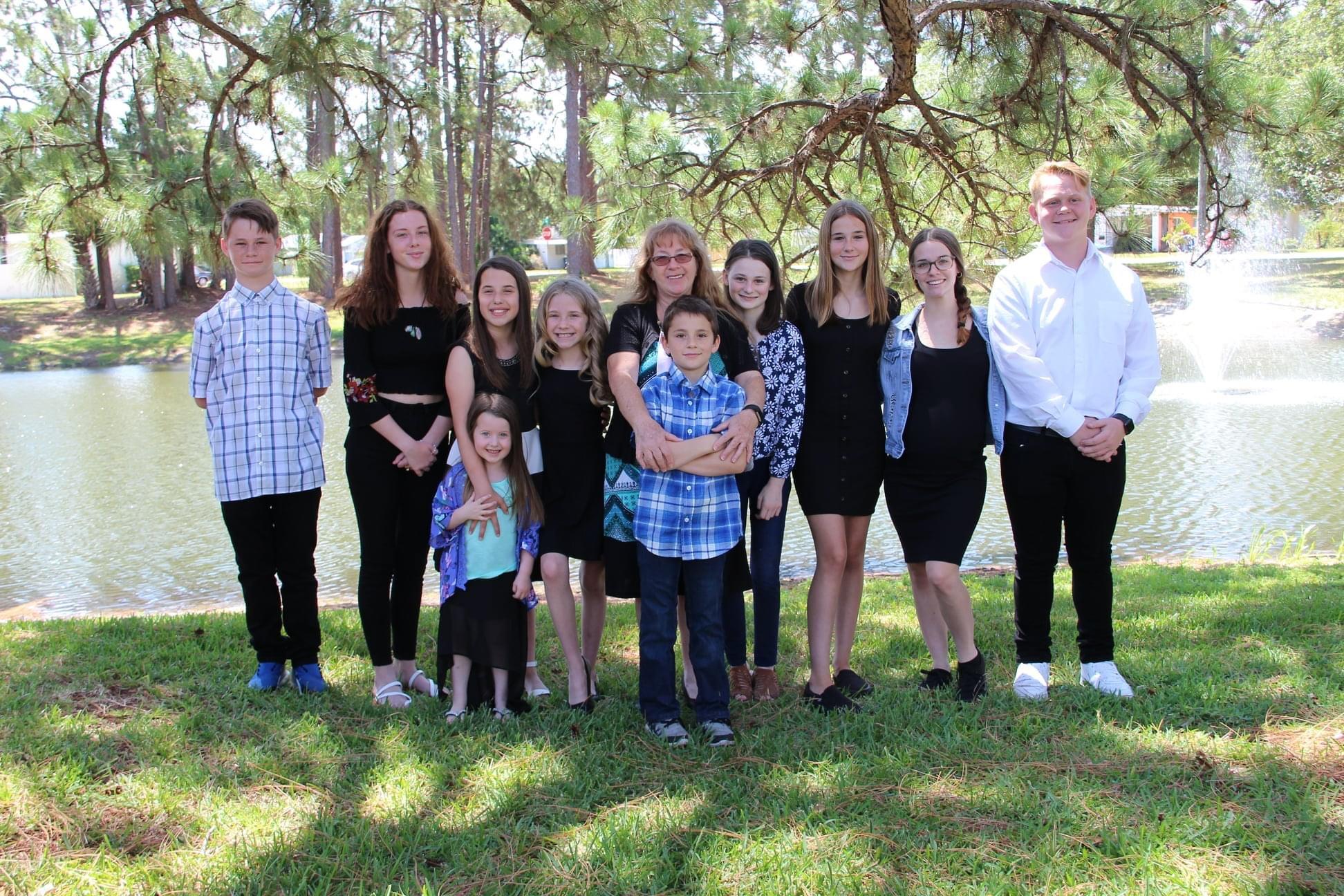 Group of family members posing together by a picturesque lake under trees on a sunny day.