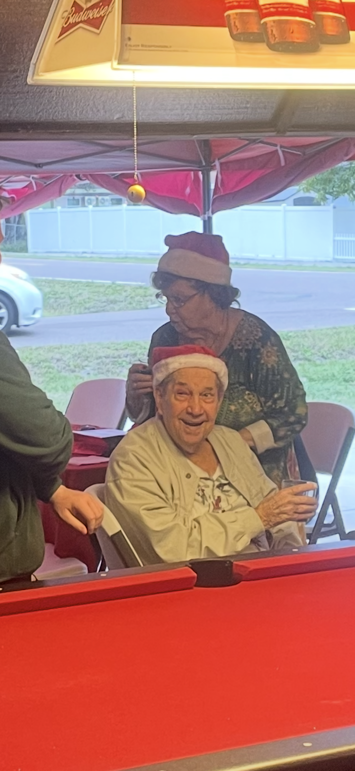 Seniors share drinks and laughter under a red canopy, celebrating a joyful occasion together.
