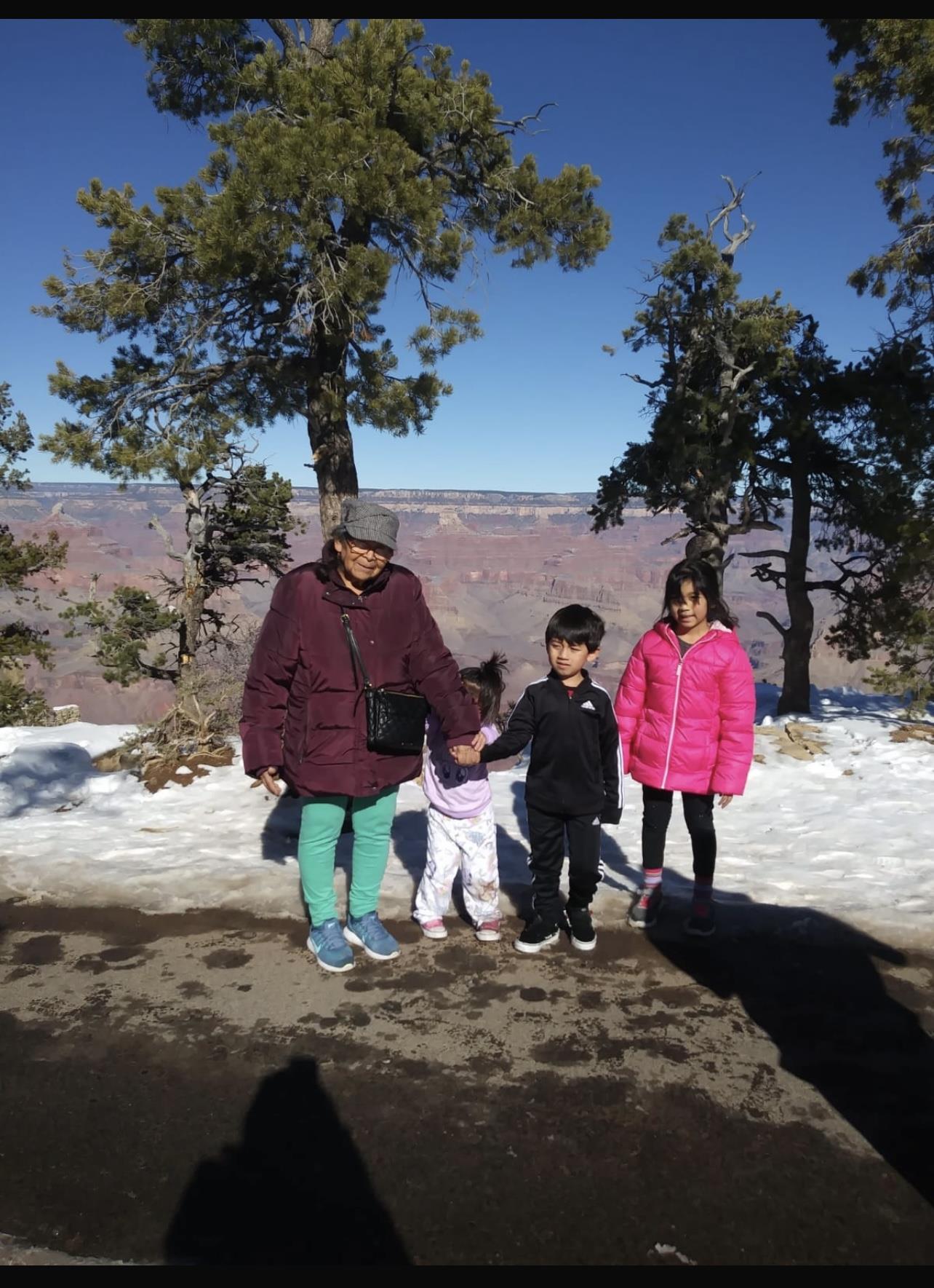 A family of four stands together at the Grand Canyon, surrounded by snow and sunshine.