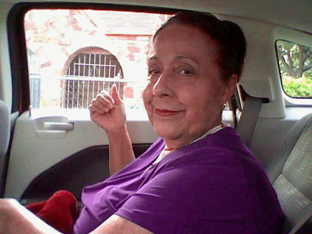Woman in a purple top smiles from the back seat of a car during a sunny city outing.