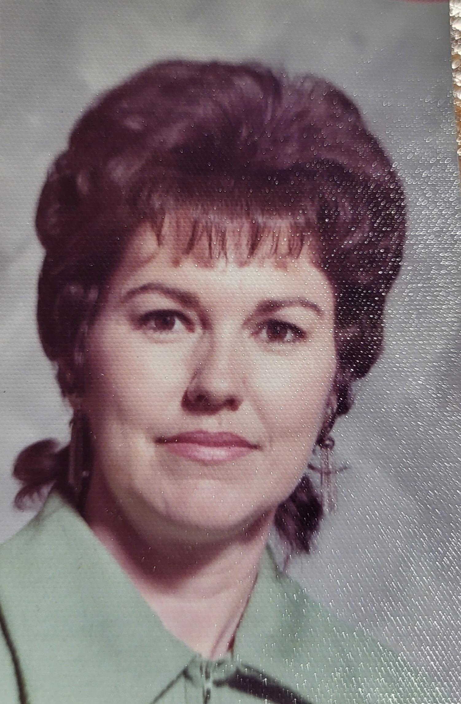 A woman with dark hair is smiling gently while wearing a green blouse, appearing thoughtful.