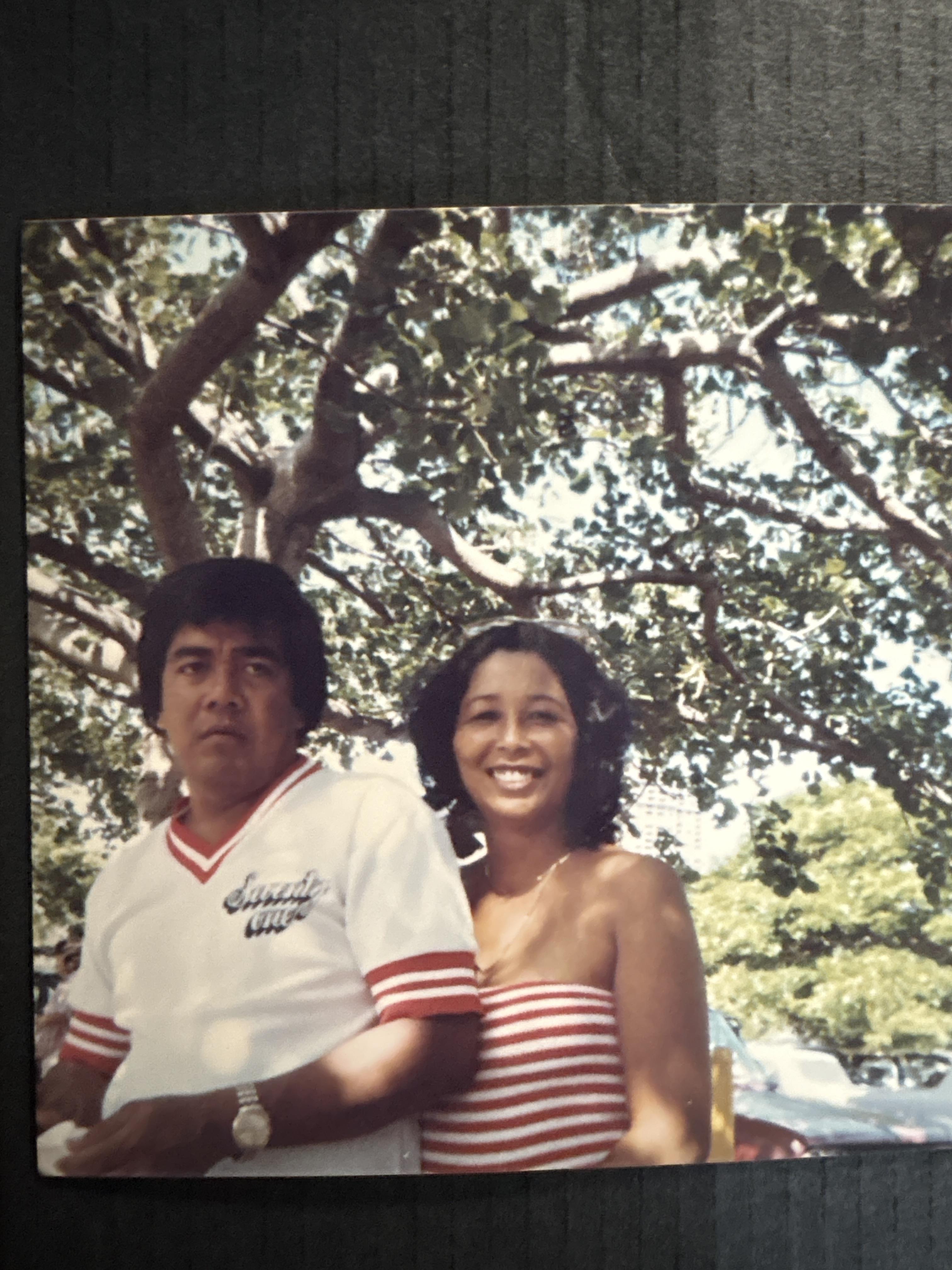 A man and woman smile at the camera while enjoying a warm day outside beneath a tree.