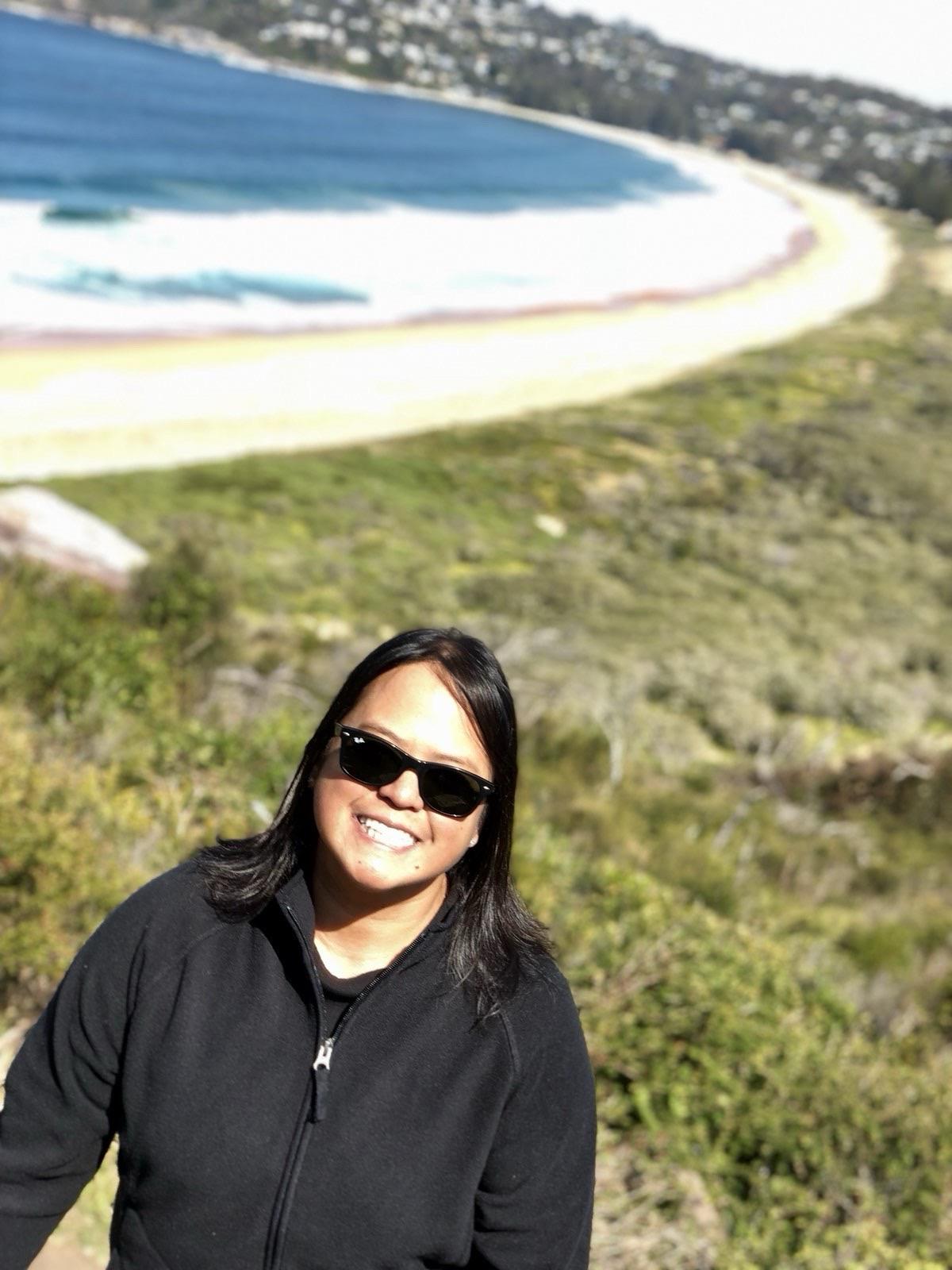Woman stands on a hillside, smiling while admiring the beautiful beach below.
