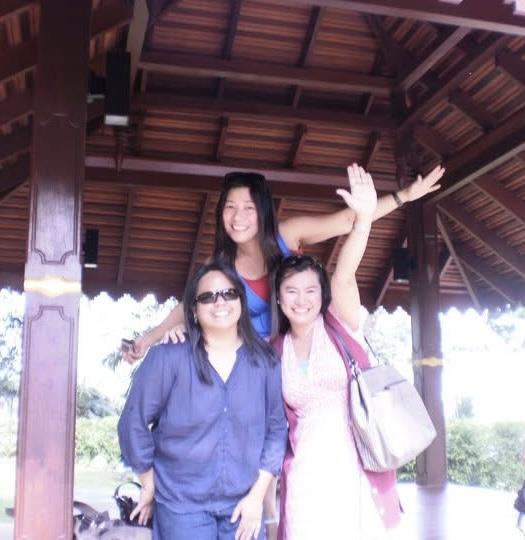 Three friends smile and pose together in a charming wooden pavilion surrounded by greenery.