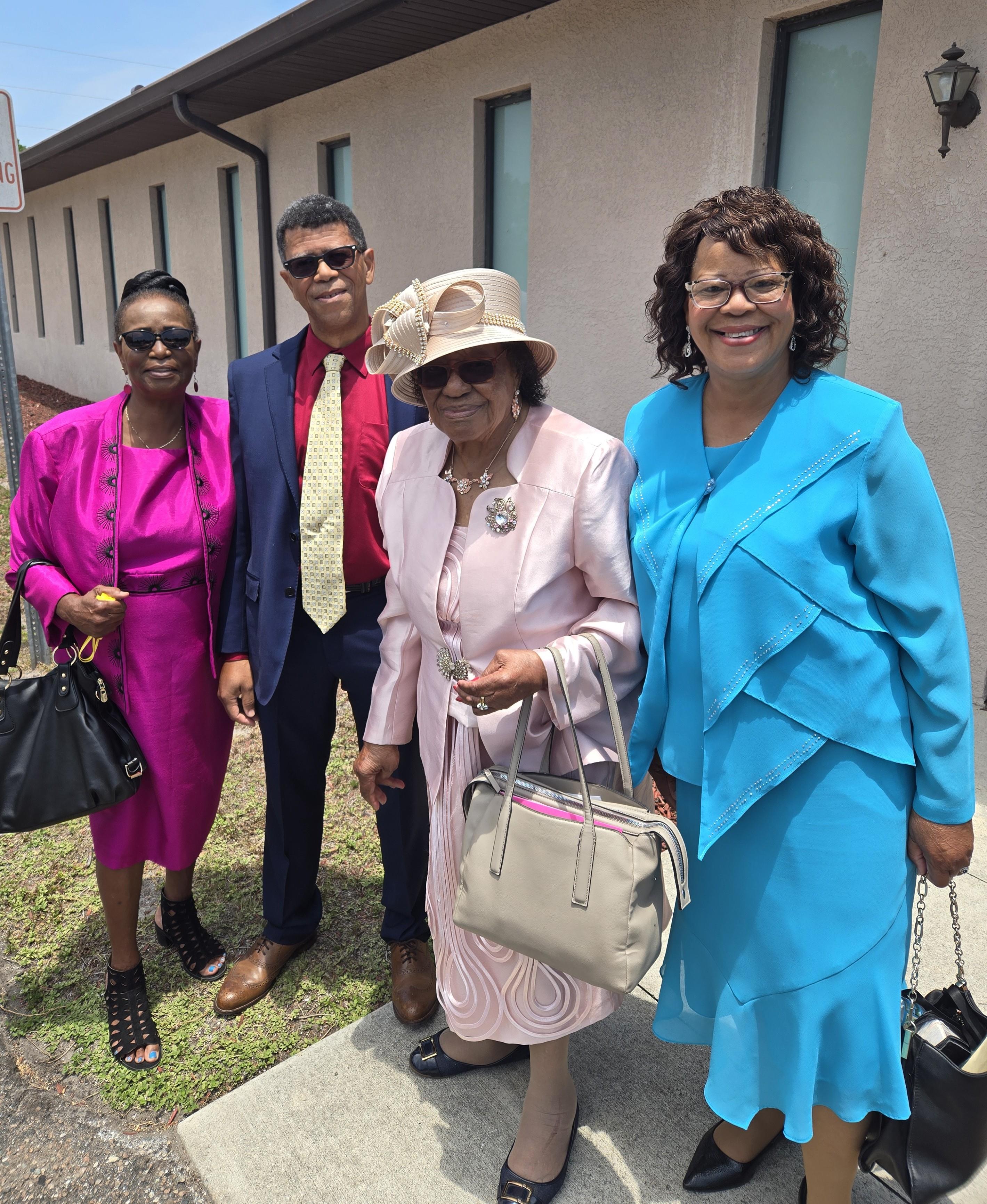 Four individuals pose together wearing colorful outfits outside a community building.