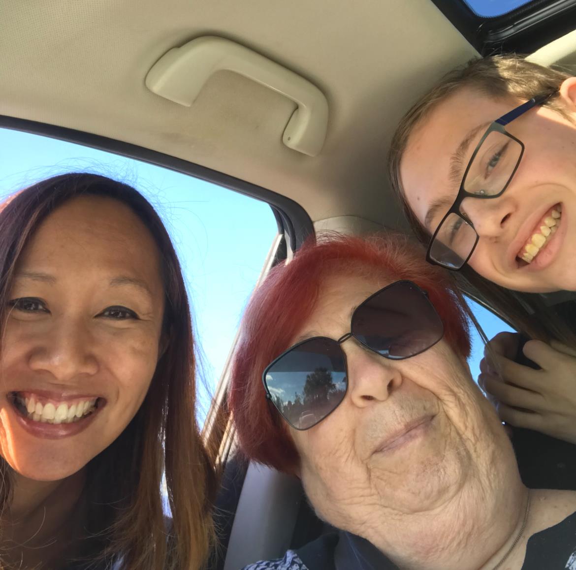 Three family members share smiles inside a car under bright sunshine, enjoying their time together.