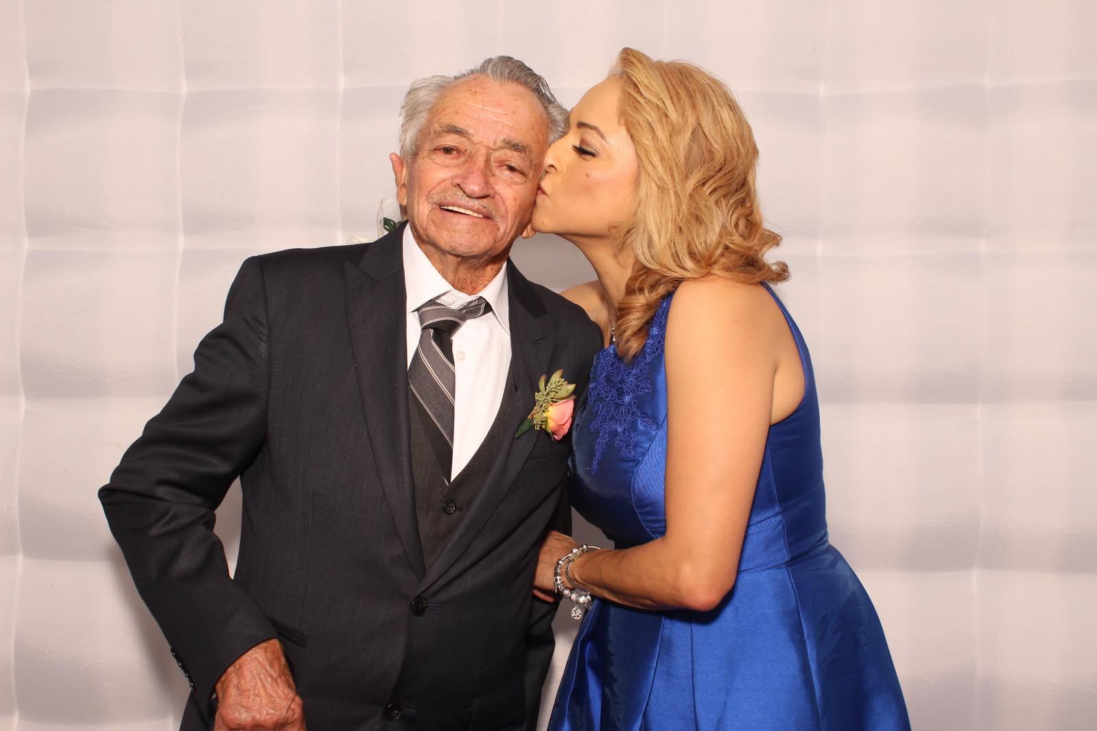 A young woman affectionately kisses an elderly man at a formal event, sharing a joyful moment.